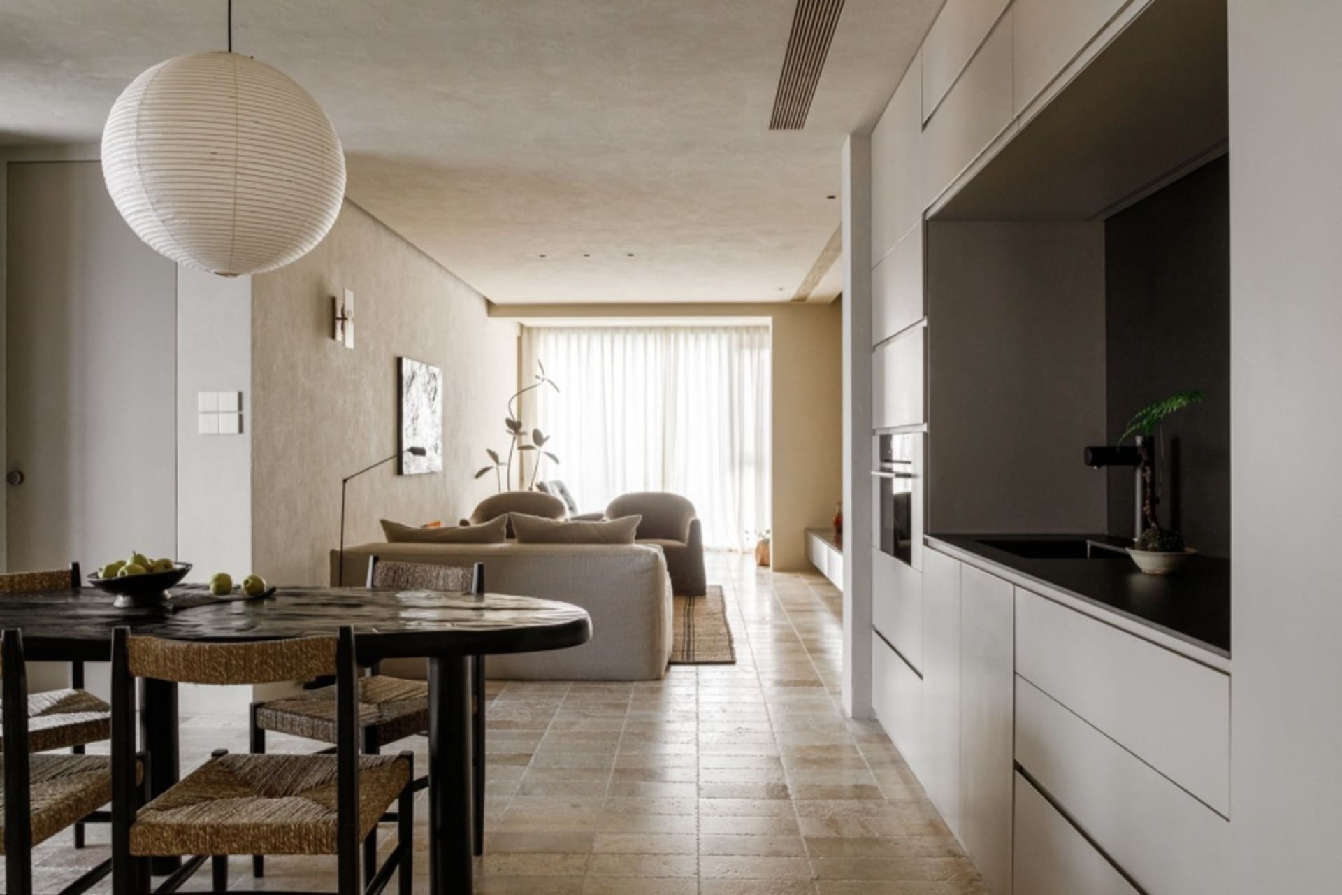 A minimalist living area with neutral-colored furniture and a sleek, modern kitchen with black accents.