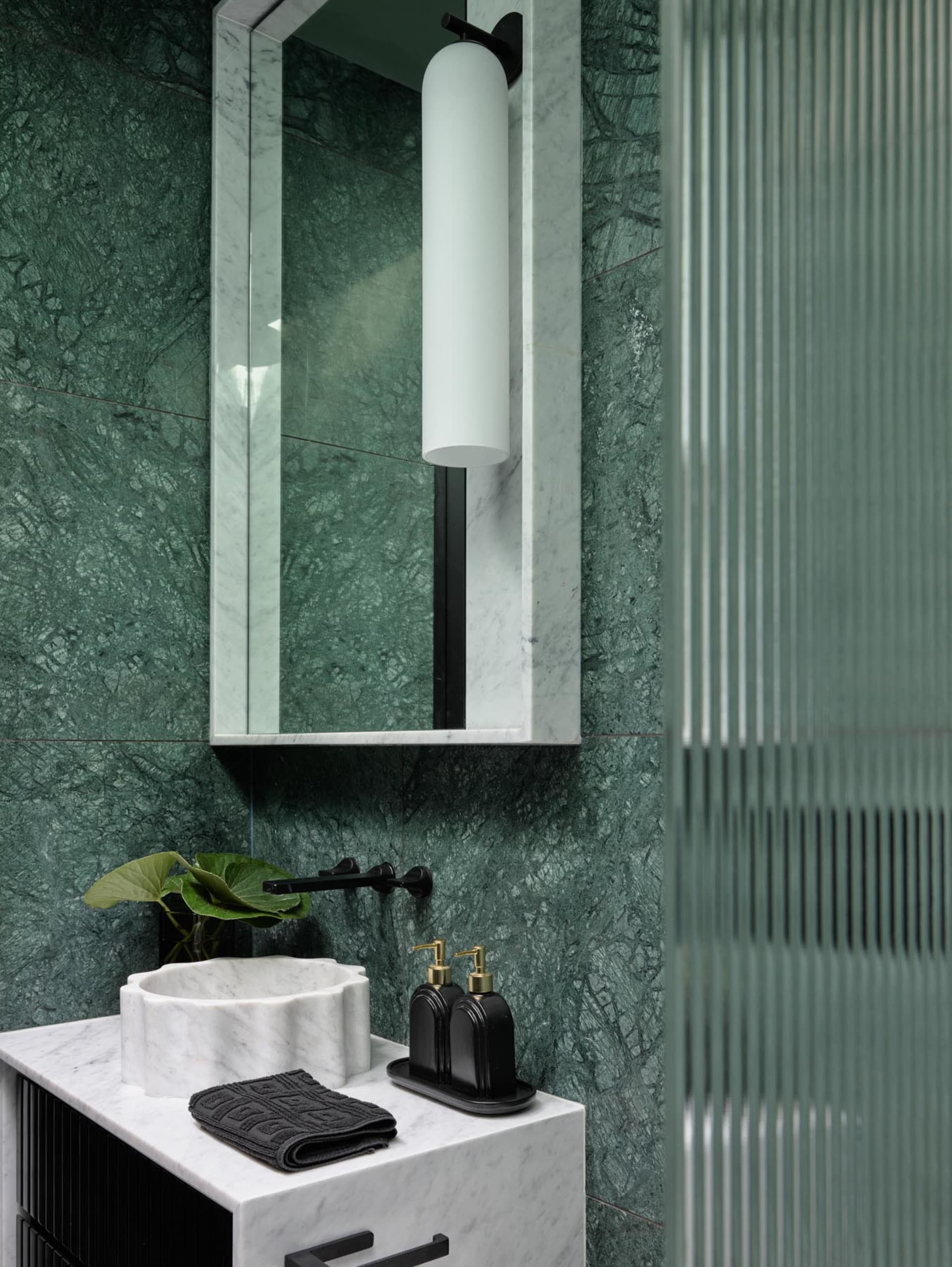 A modern bathroom with green marble walls, a glass shower enclosure, and black and white checkered floor tiles.
