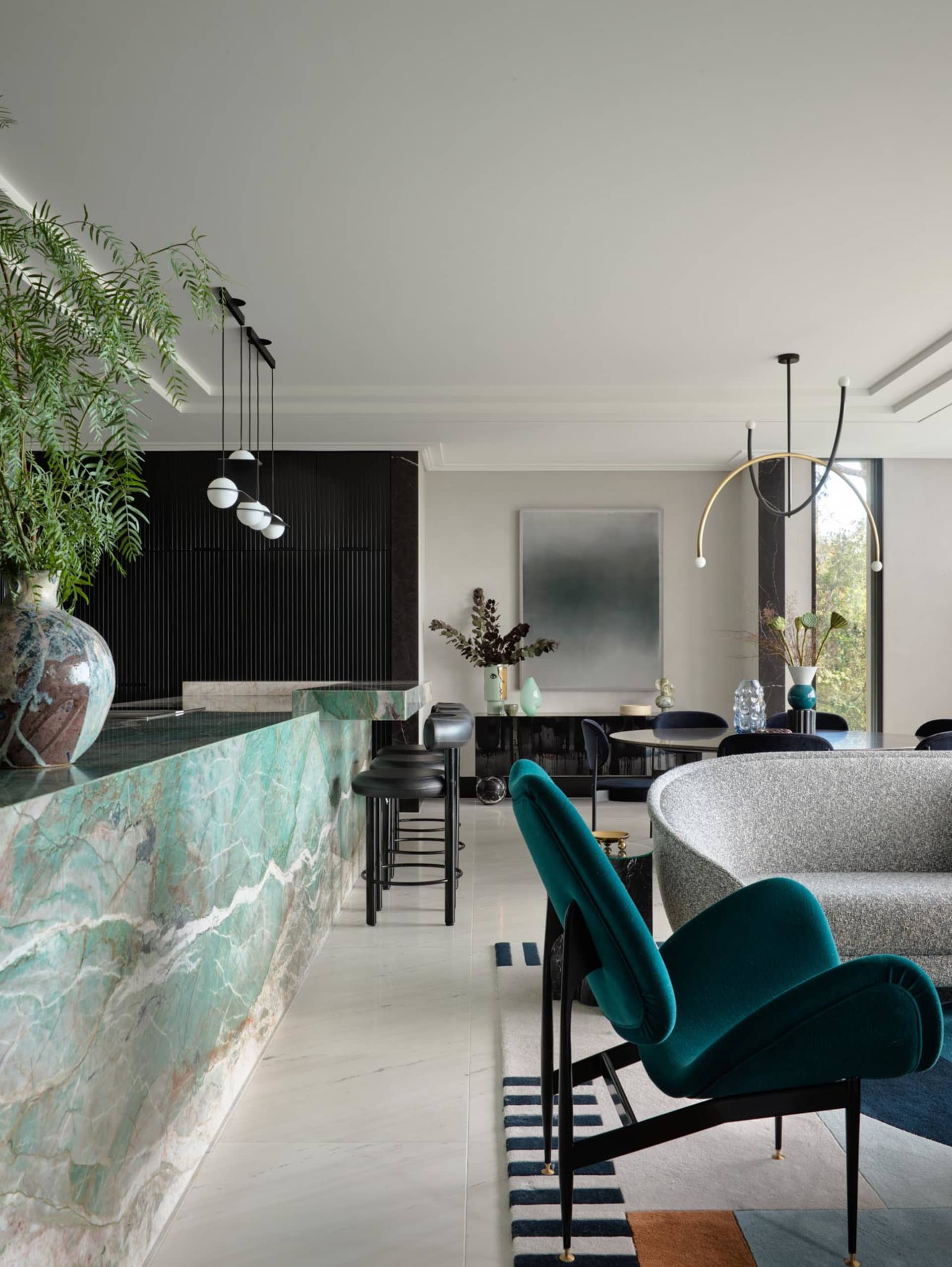 Modern living room with a marble counter, green upholstered chair, and glass dining table.
