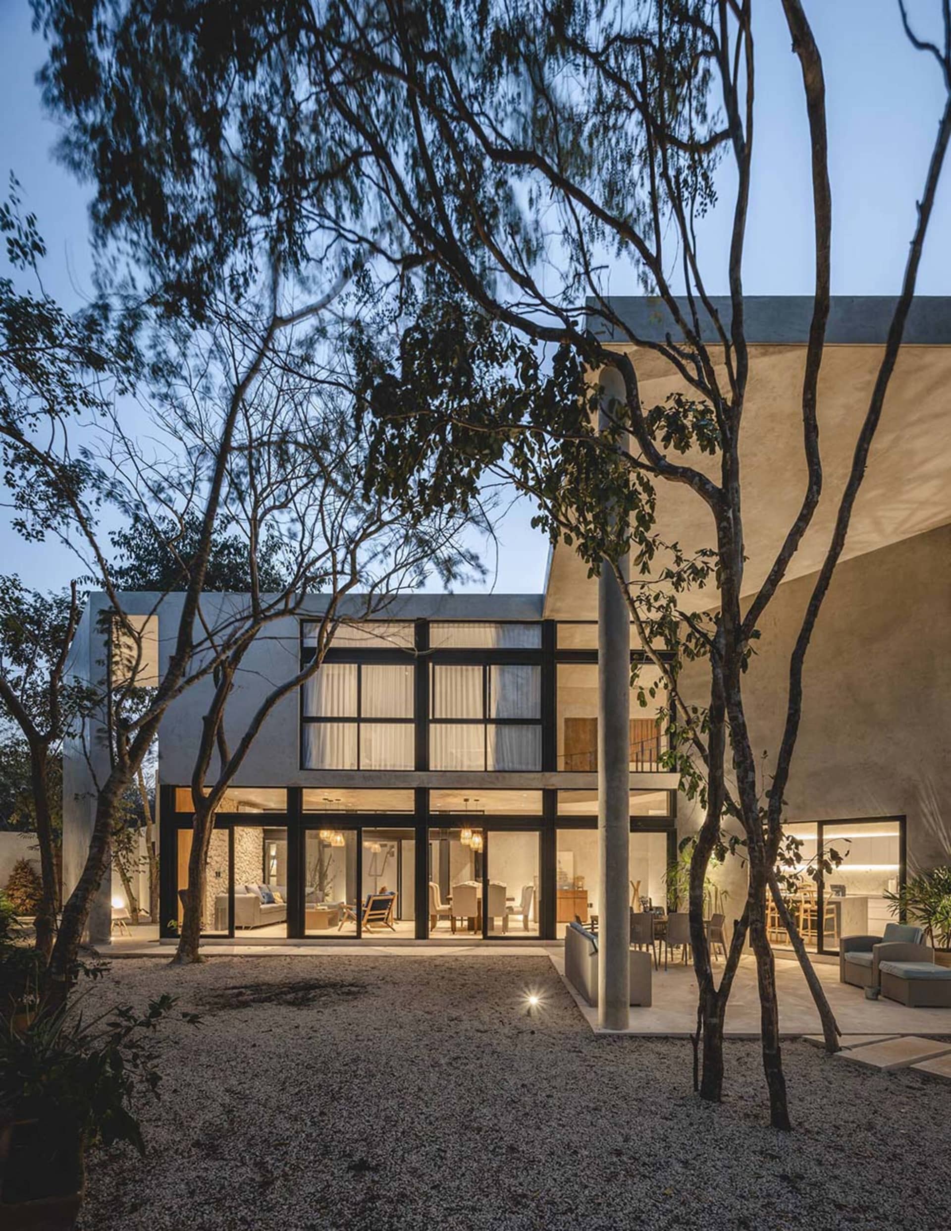 A modern residential interior with concrete walls and floors, featuring a spacious living room and a well-lit dining area.