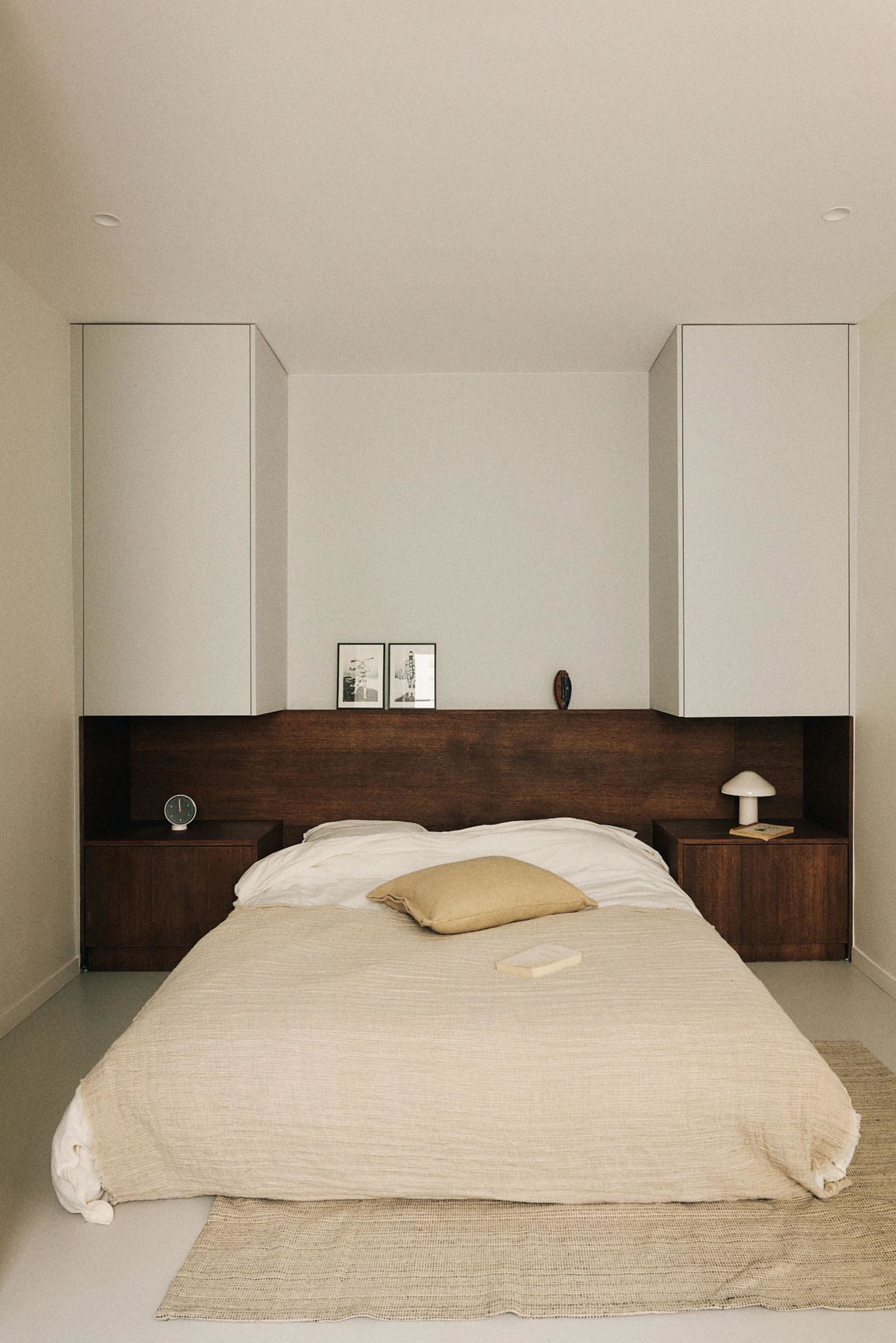 A minimalist bedroom featuring a comfortable bed with a textured fabric cover, two side tables, and integrated storage soluti