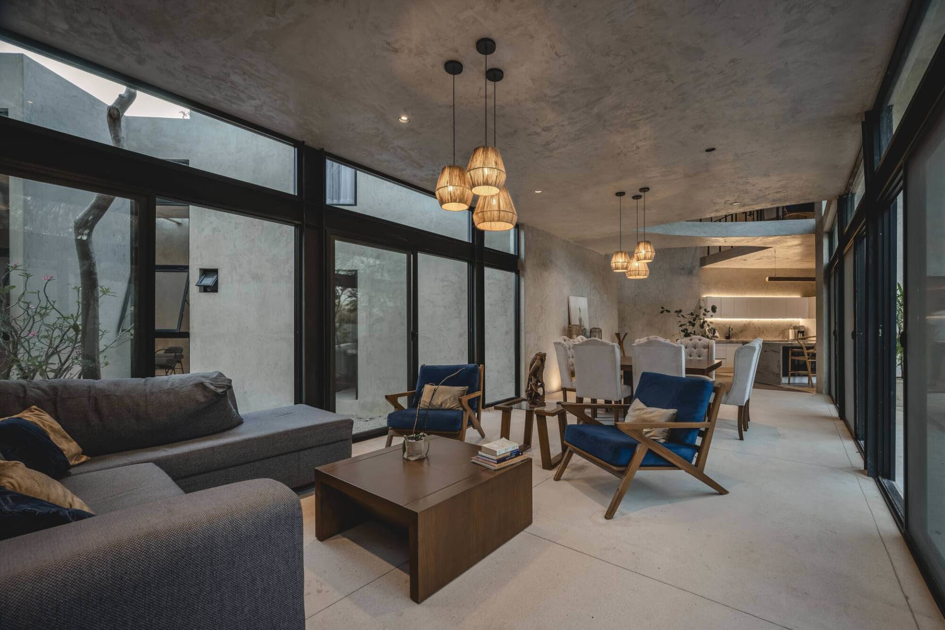 Minimalist living room with concrete flooring and furniture, modern pendant lights, and large windows.