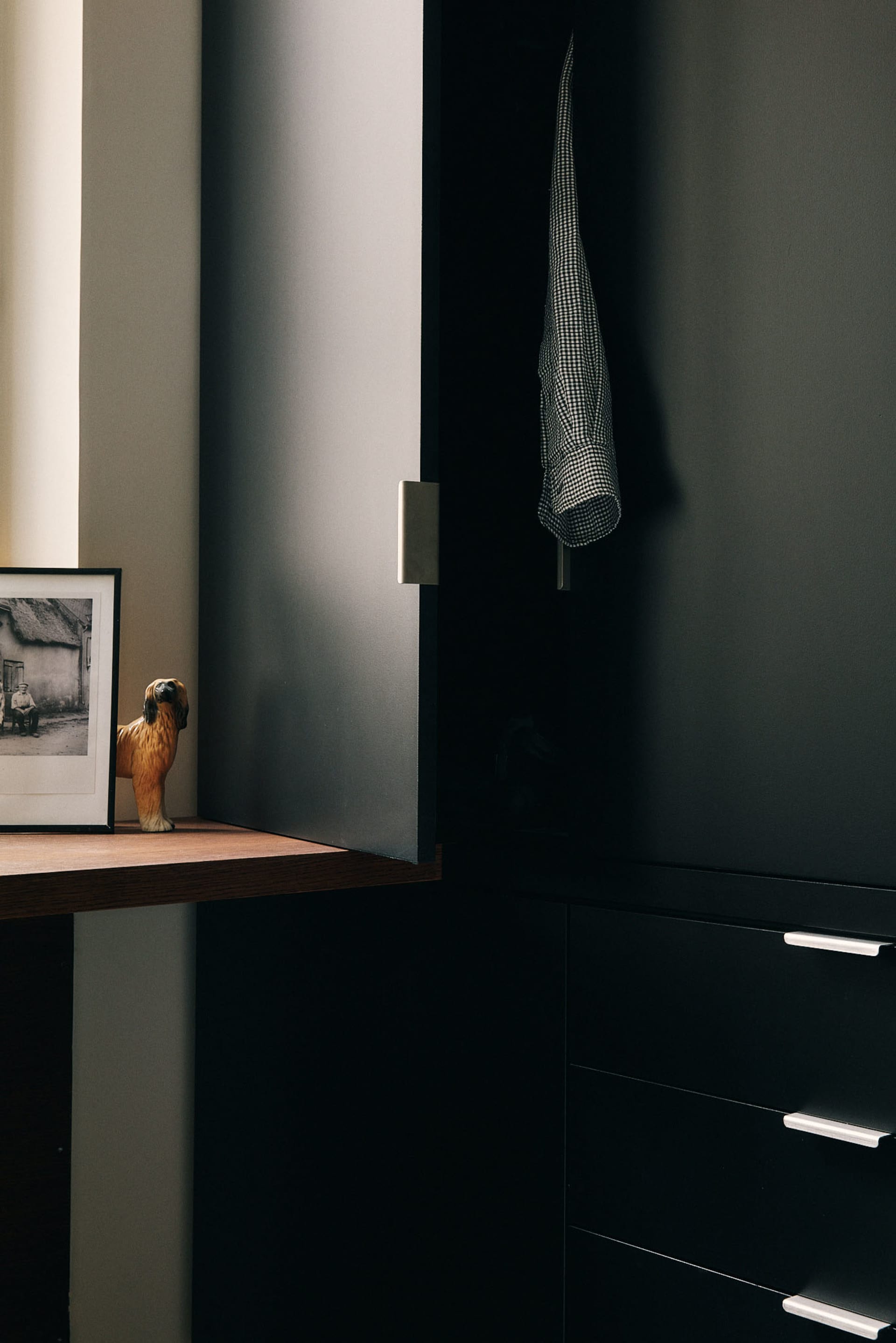A modern black metallic closet with a checkered shirt hanging inside, a wooden ledge displaying a figurine, and a framed phot