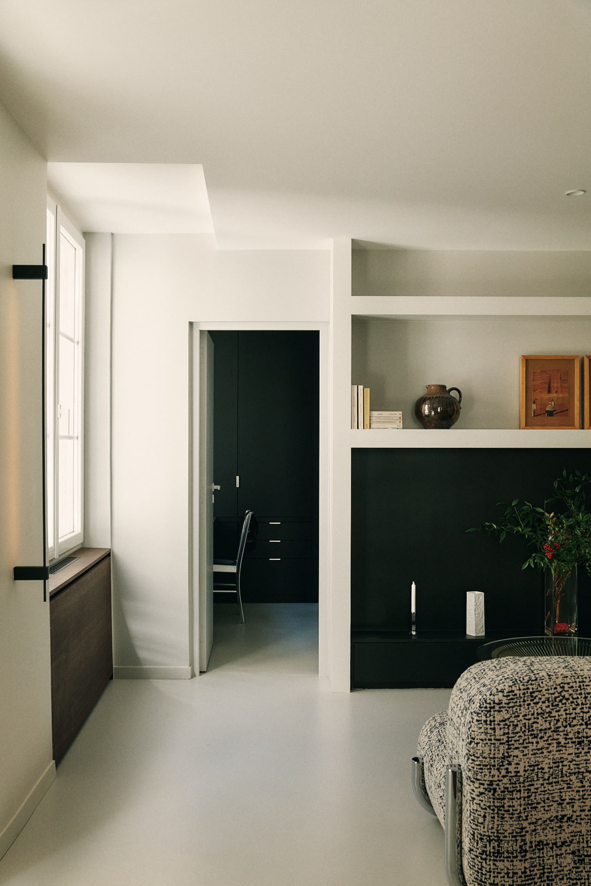 A minimalist living room with neutral tones, featuring a white sofa and black floating shelves.
