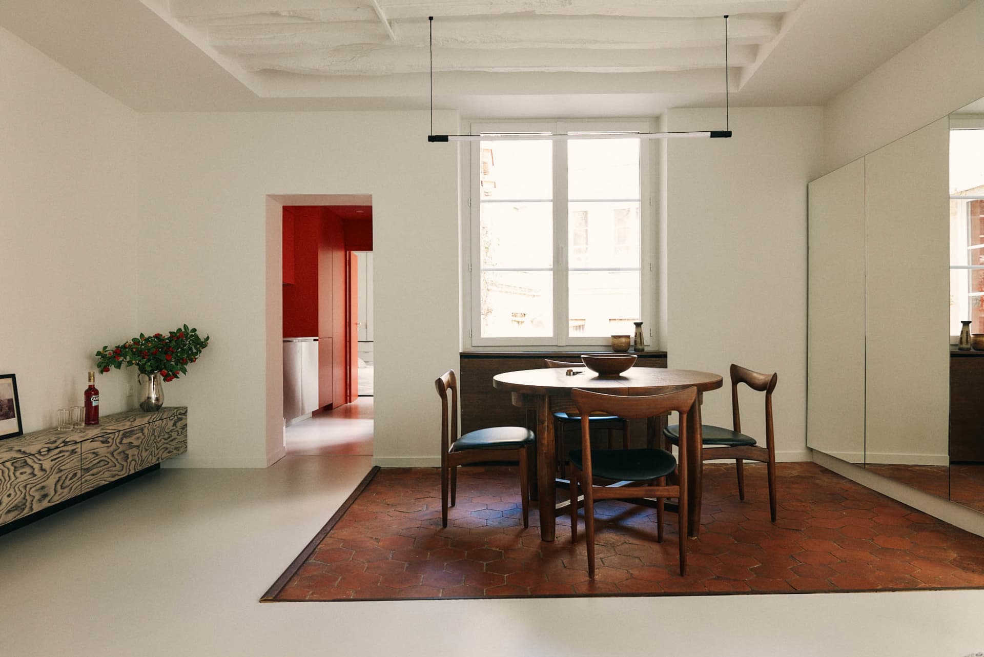 A modern dining room with a round wooden table, black chairs, and a hanging light fixture.