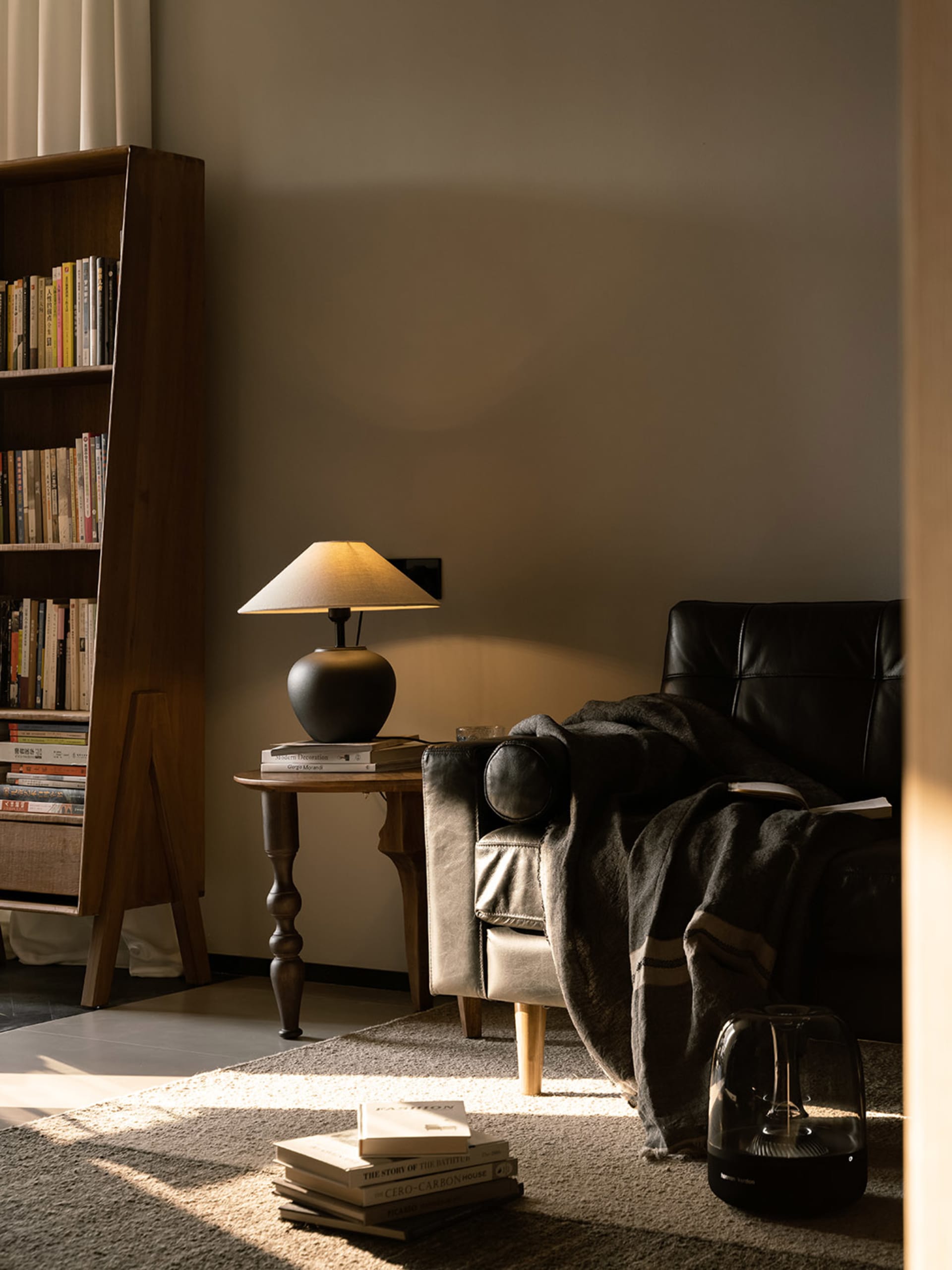 A minimalist living room featuring a wooden armchair, a lamp, and a bookshelf filled with books.