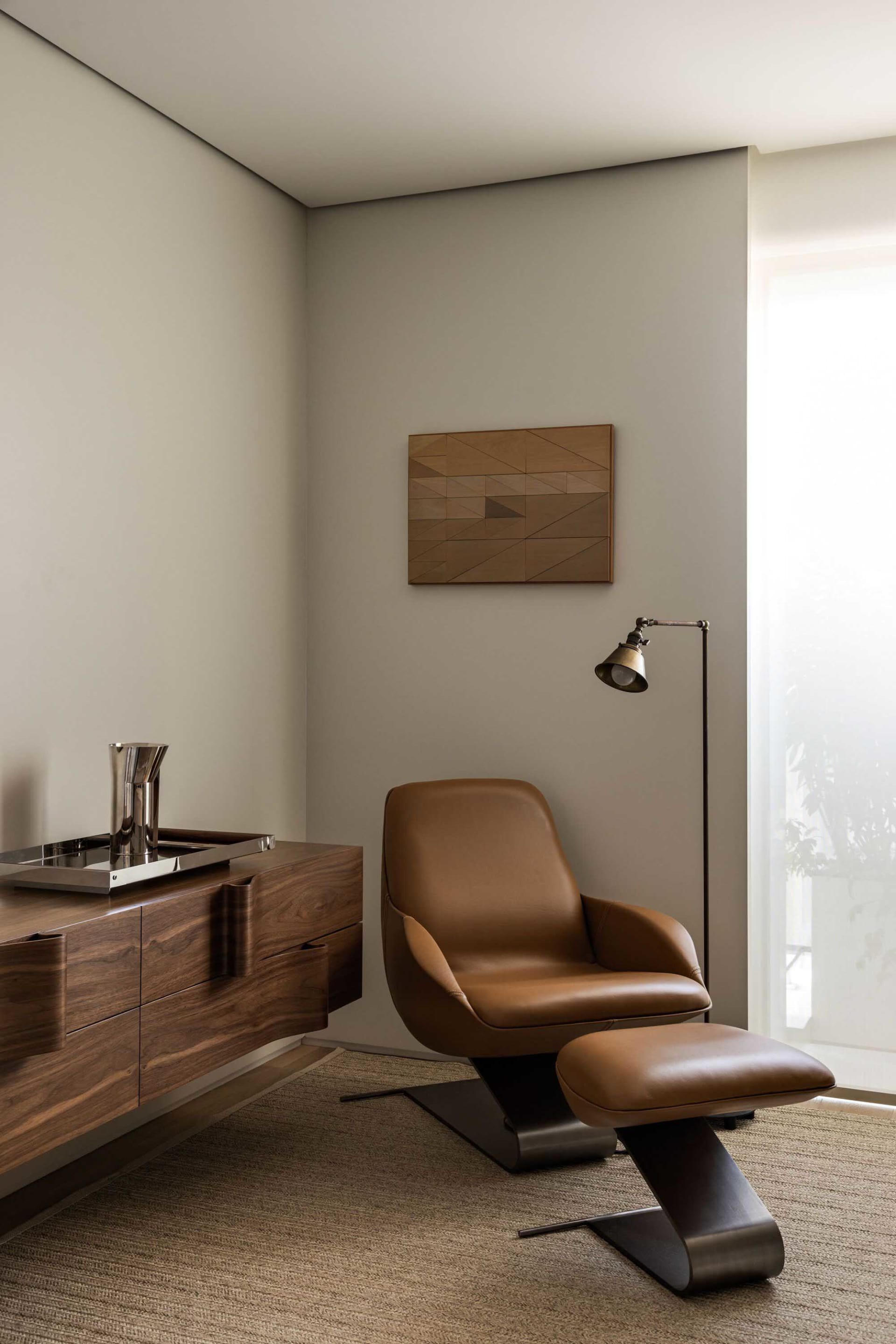 Modern living room with a brown leather armchair and metallic floor lamp, featuring a geometric wall art.
