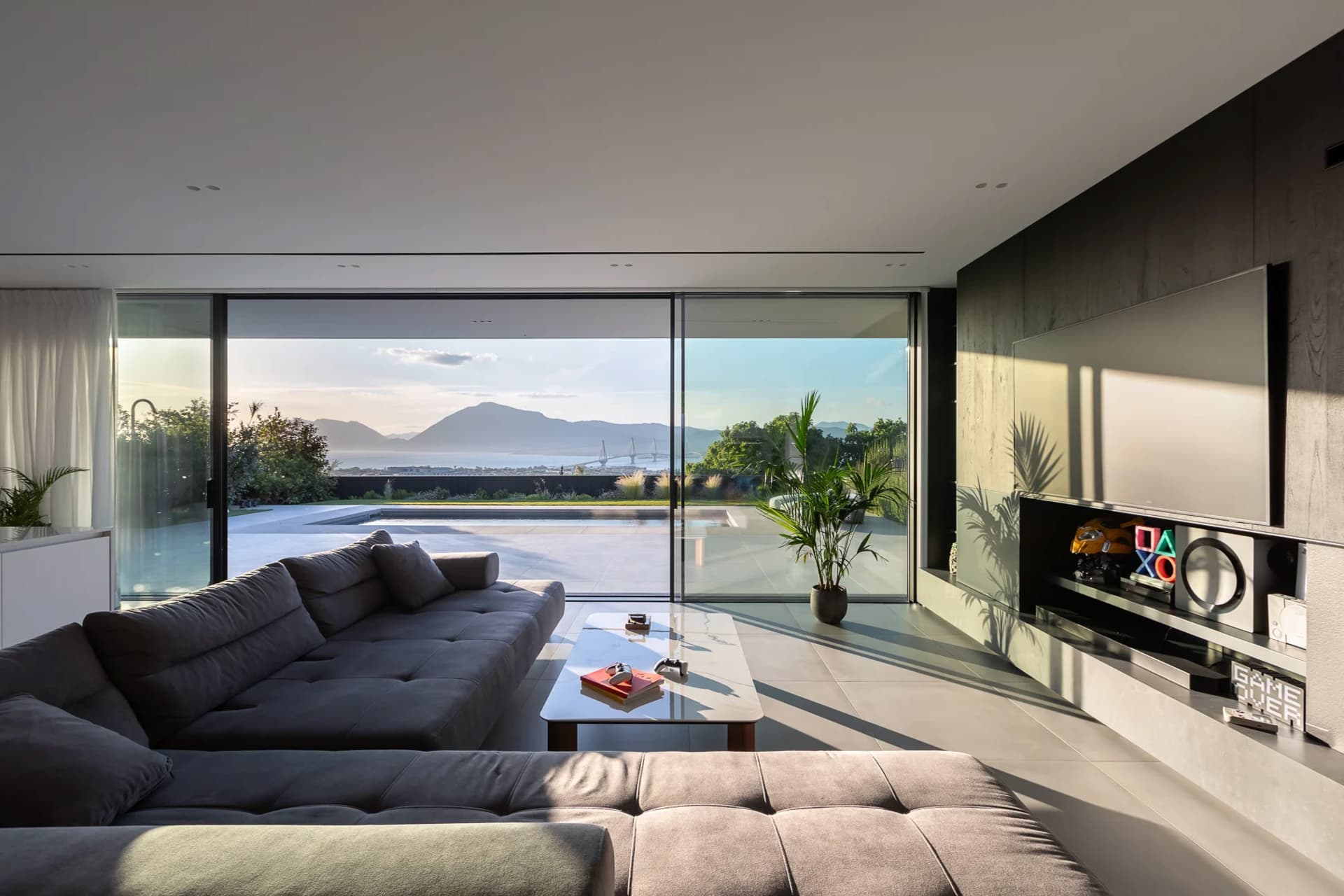 A modern minimalist living room with large glass walls and concrete flooring, featuring a spacious sofa and a sleek, minimali