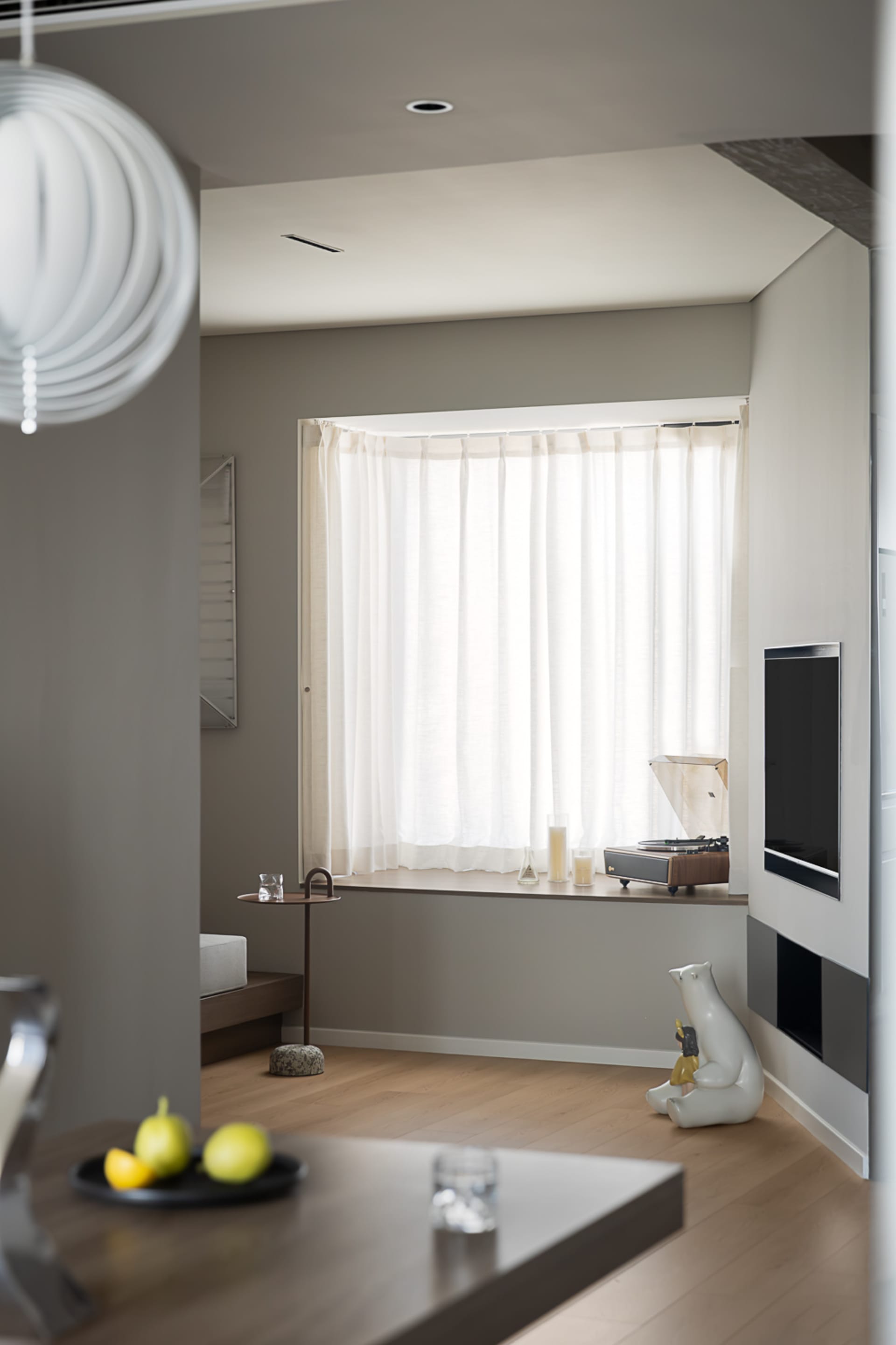 A minimalist living room featuring white curtains and polished wooden floors.