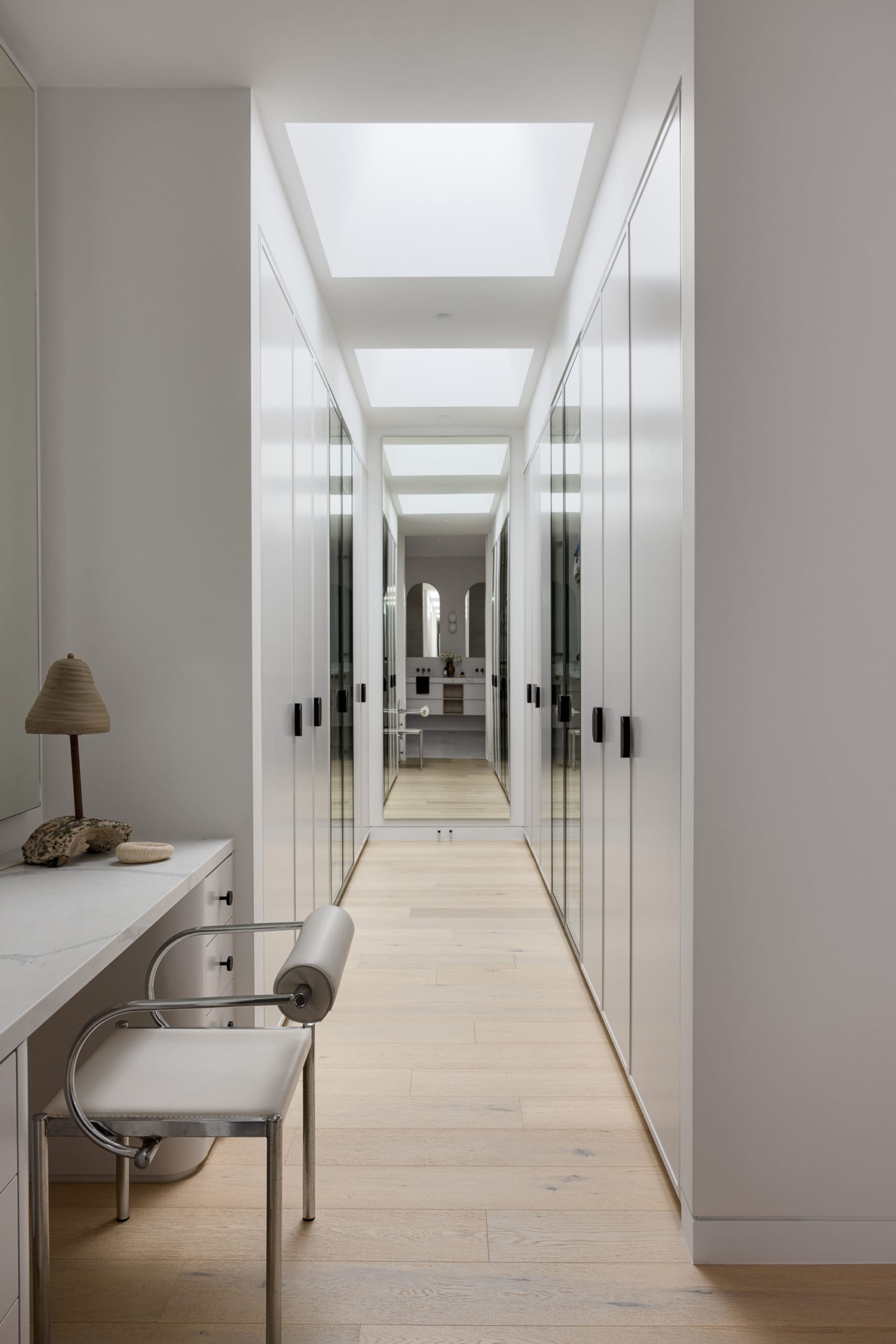 A minimalist white closet with mirror doors and a long hallway