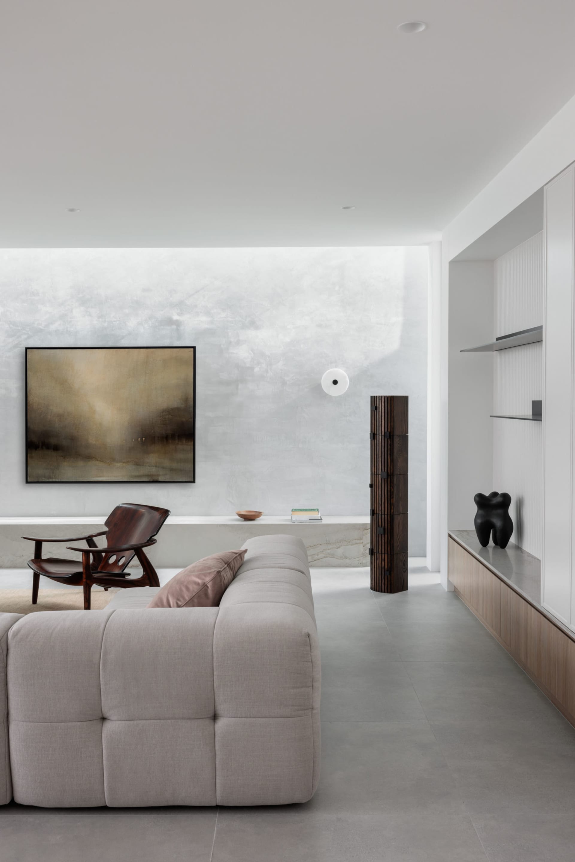A modern interior design of a living room featuring a concrete wall, minimalist furniture, and abstract art.
