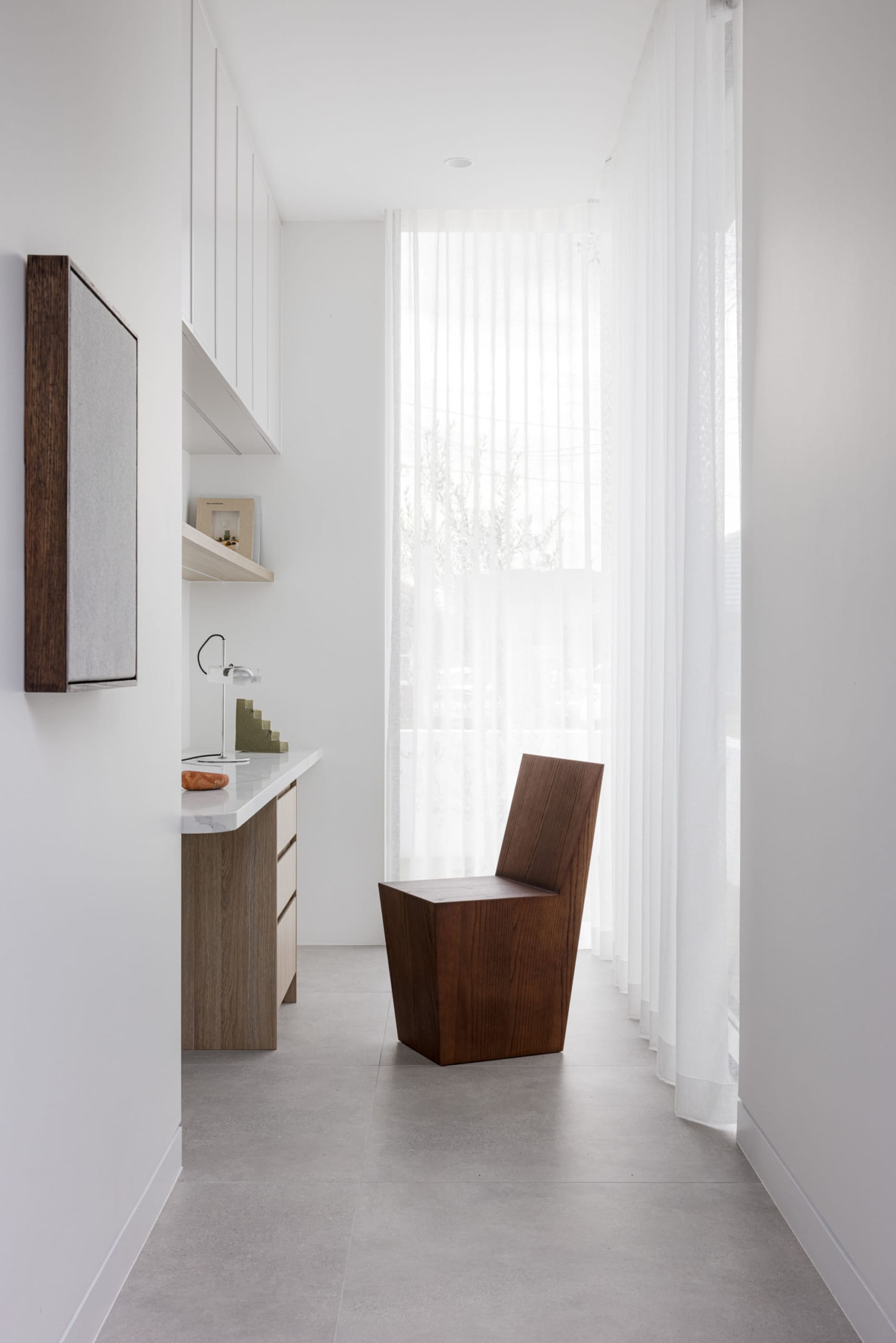 Modern residential interior featuring a wooden chair, a glass wall, and concrete flooring.