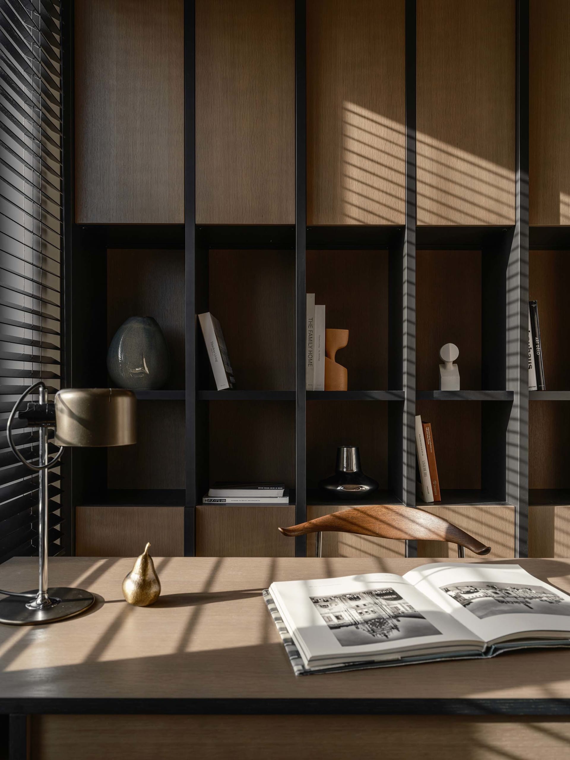 A minimalist home office library with a wooden desk, metal chair, and bookshelf.