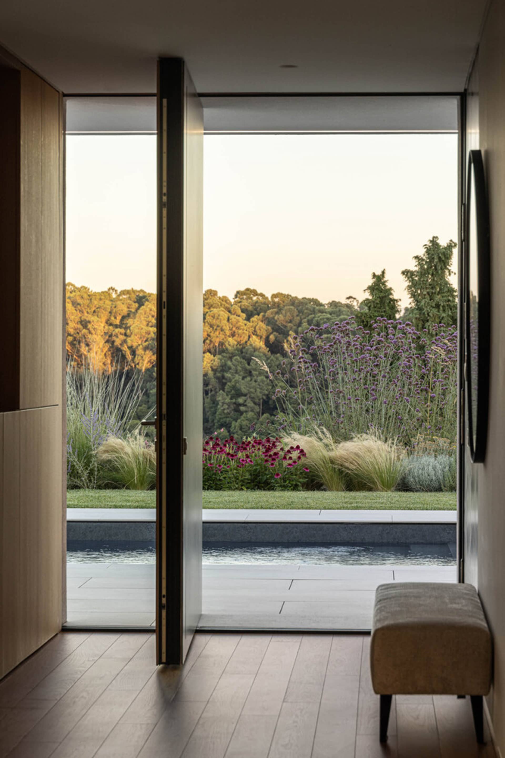 Modern exterior with large glass doors, pool, and lush garden view at dusk.