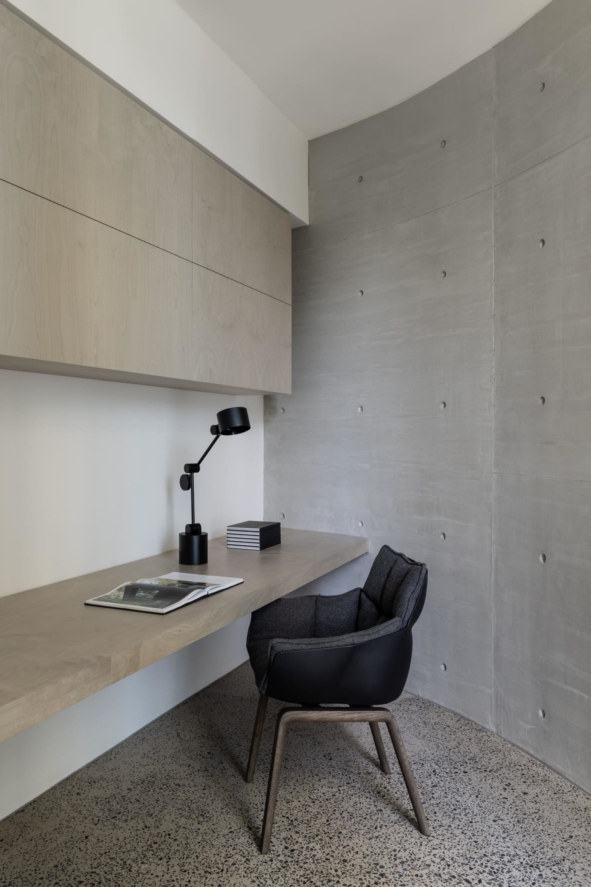 A modern, sleek workstation with a wooden desk and black lamp positioned against a concrete wall.