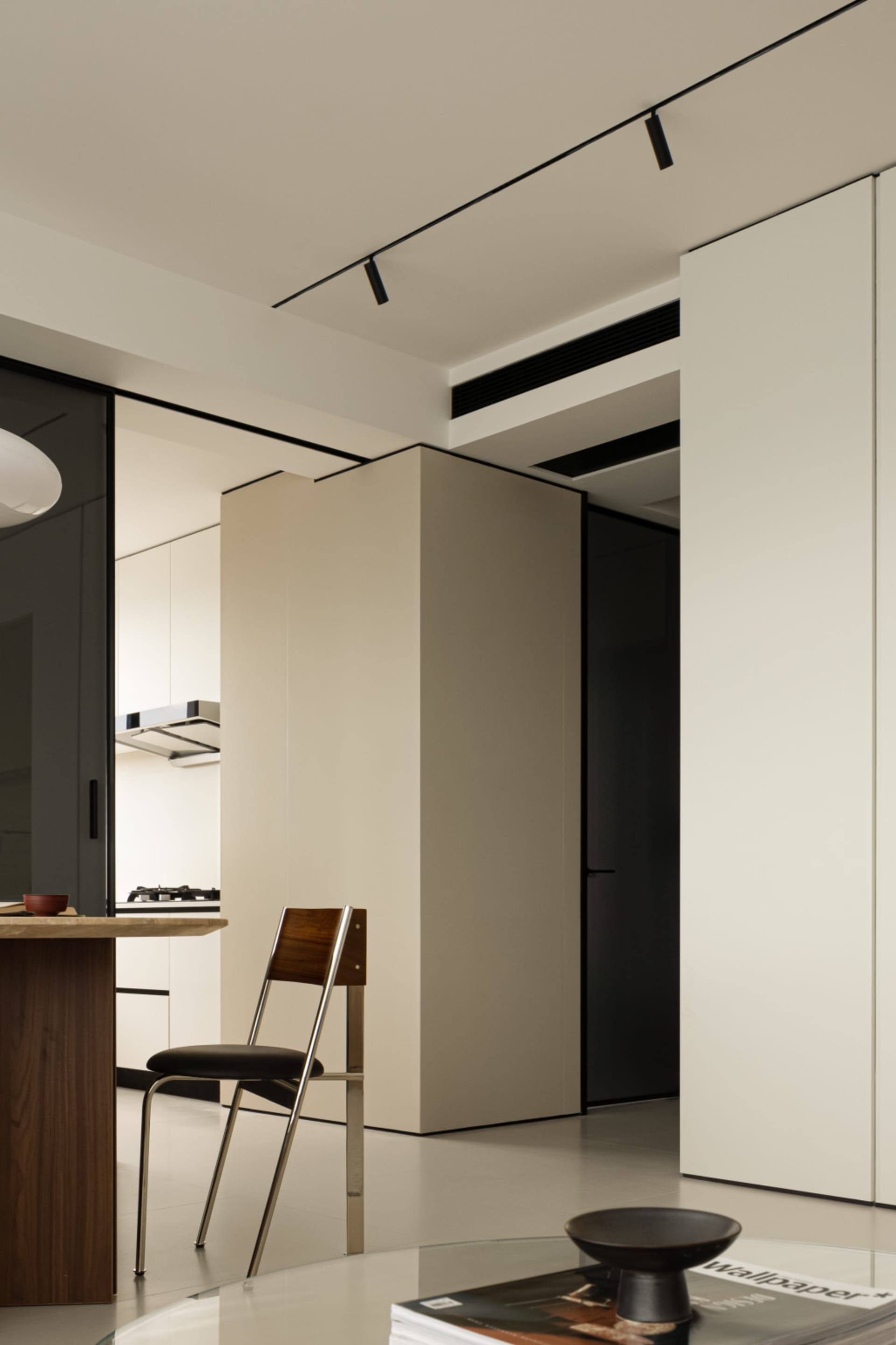 A modern minimalist living room with a concrete open-plan design, featuring a sleek wooden dining table and a black chair.