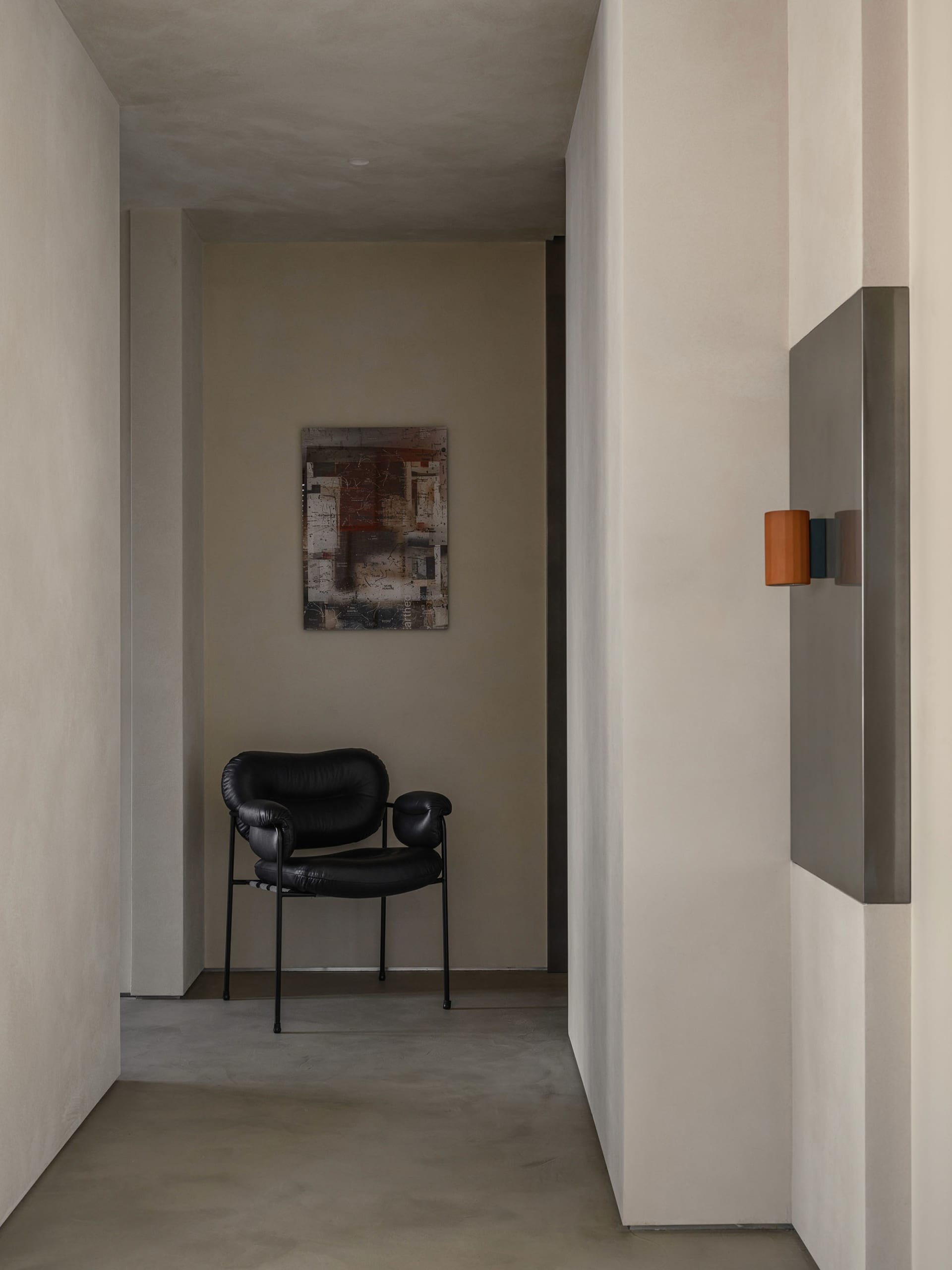 Modern interior design featuring a minimalist concrete wall with a sleek black armchair and a contemporary art piece.