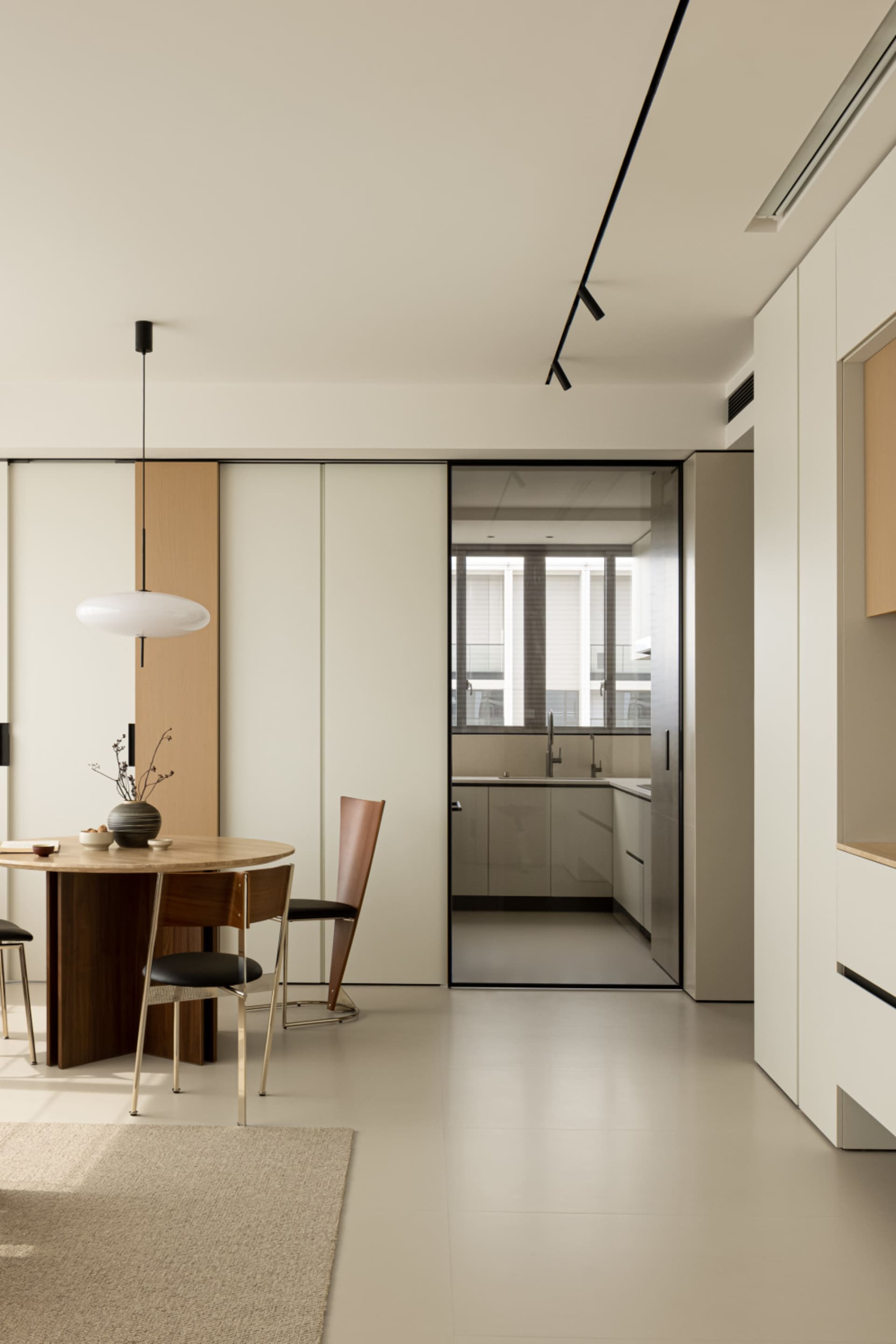 A modern minimalist kitchen with white laminate cabinets and a white pendant light fixture.
