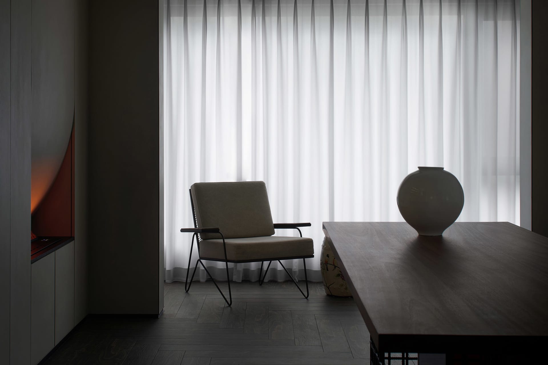 An elegant, minimalist living room features textured cotton curtains, wooden furniture, and a comfortable armchair against a