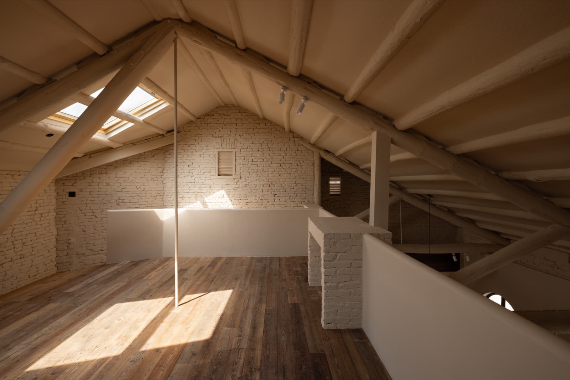 Modern minimalist attic space with exposed wooden beams, brick accents, and a skylight allowing natural light to enter.