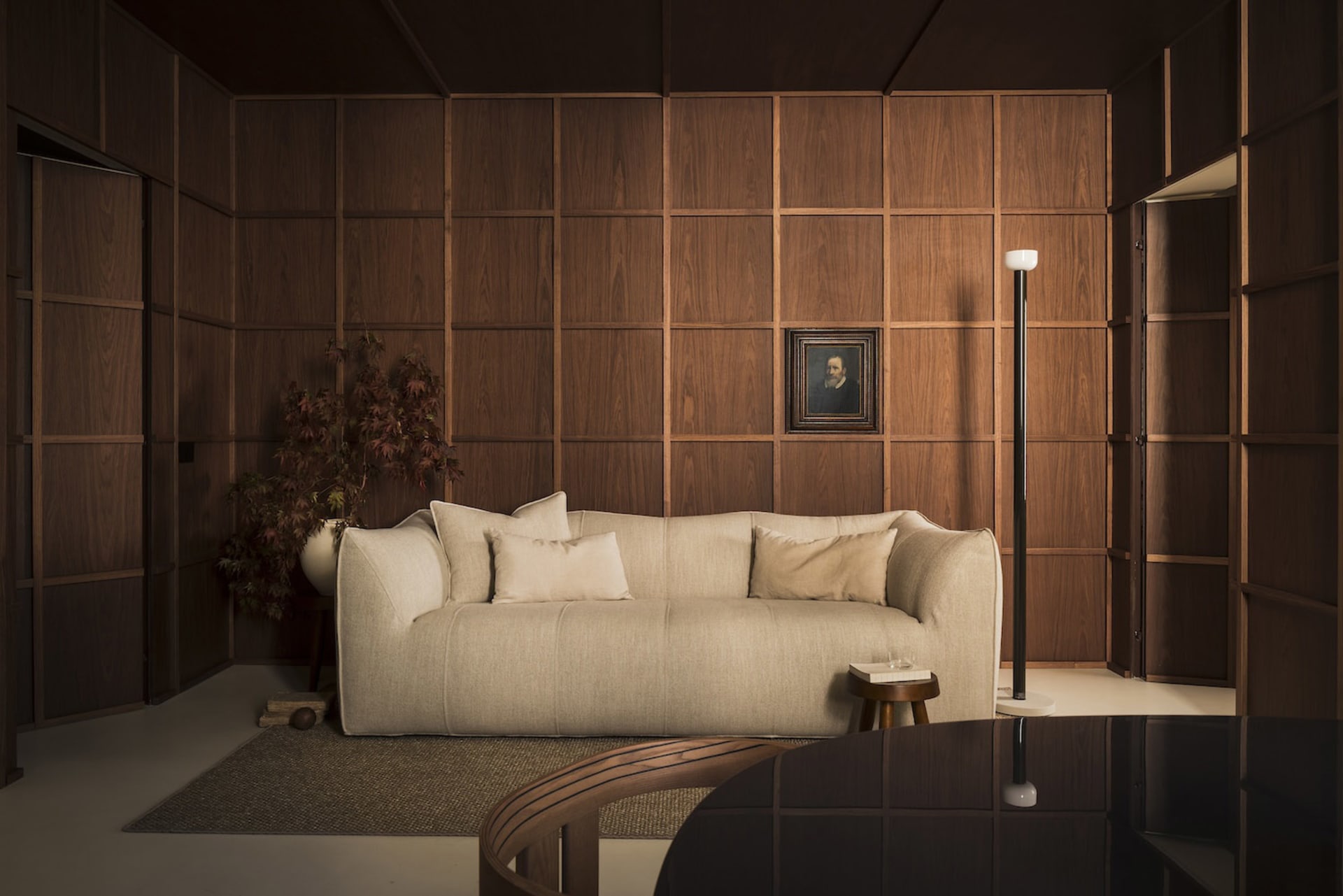 A cozy living room featuring a beige sofa, wooden panel walls, and a framed portrait.