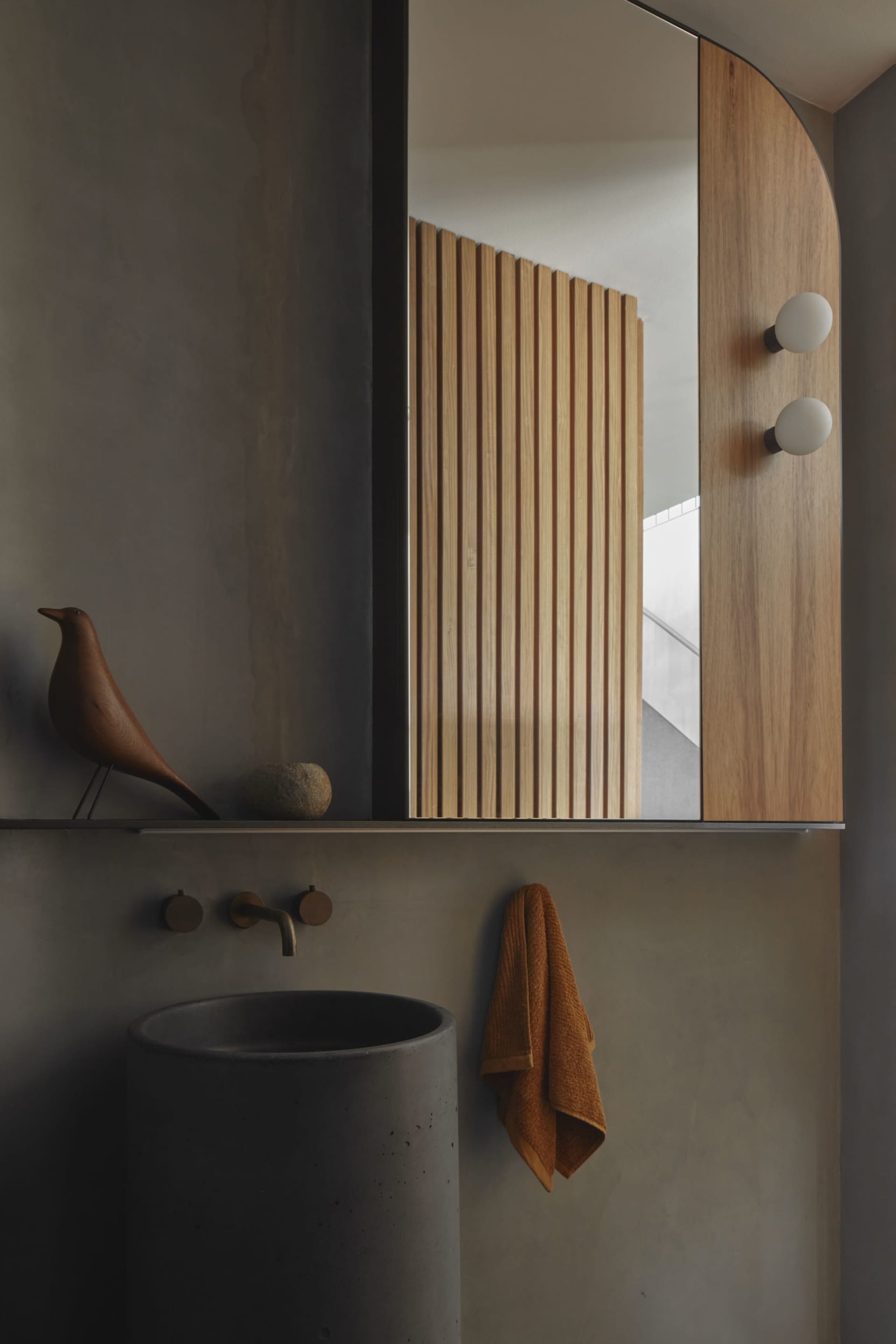 A modern bathroom featuring a concrete sink, wooden slat partition, and minimalist decor.