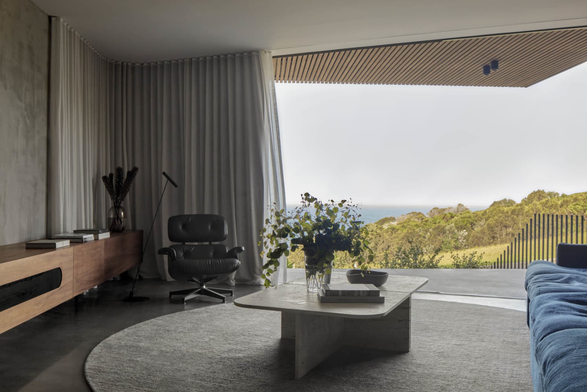 A modern living room featuring a concrete floor, minimalist furniture, and a view of the ocean through large windows.