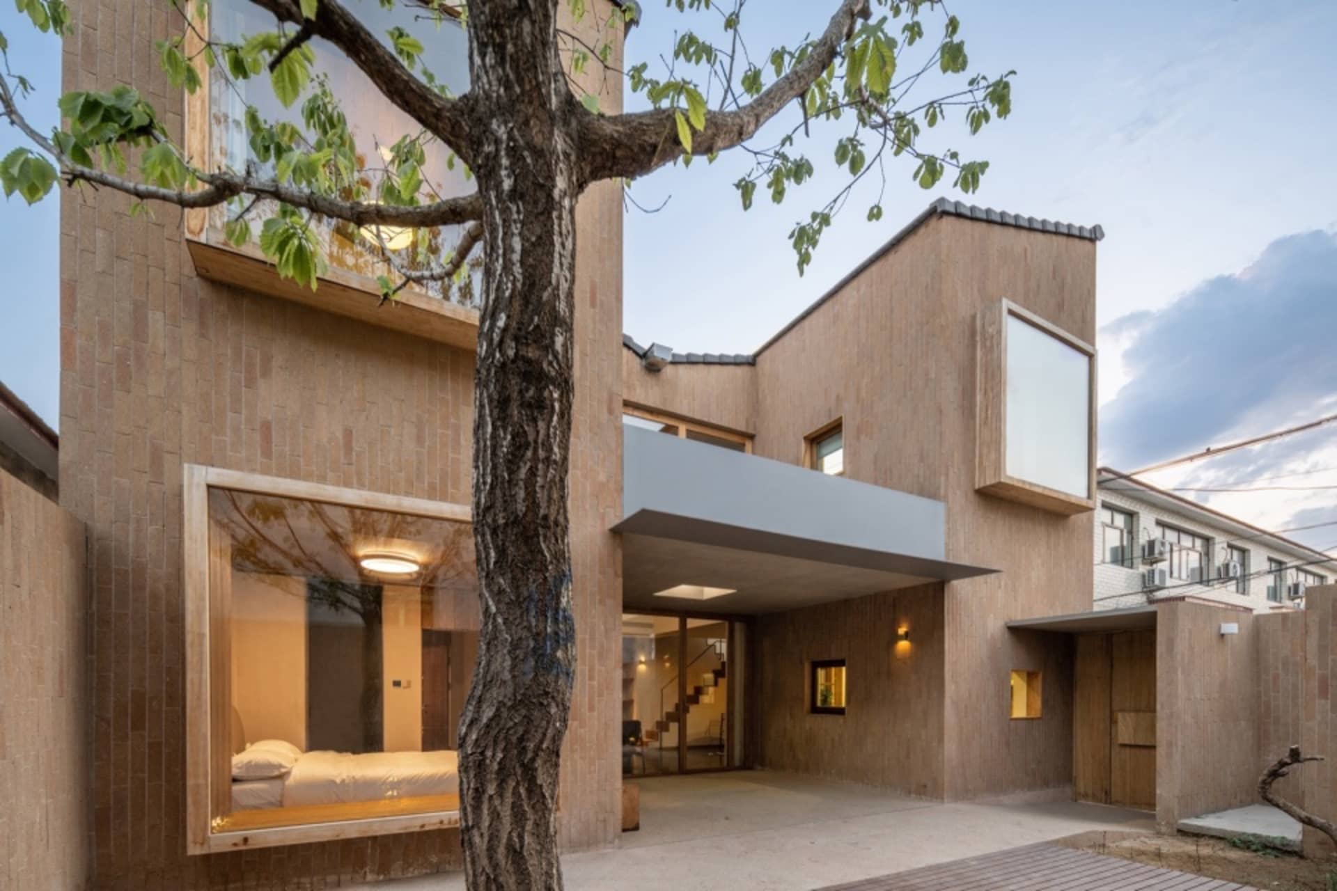 一座以木質材料建造的現代住宅建築,擁有大面窗戶,前景有一棵樹。