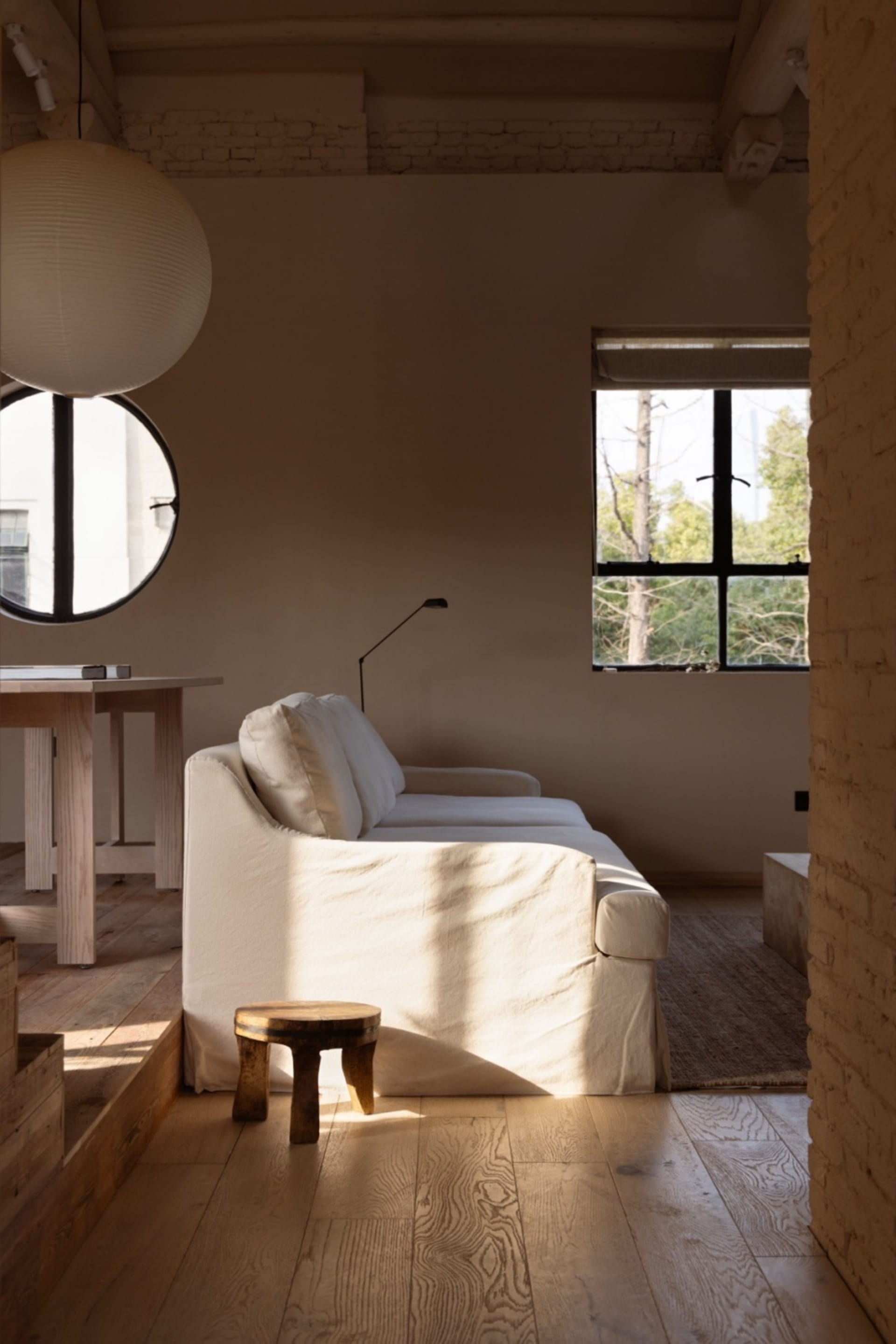 A minimalist living room featuring wooden furniture, a white couch, and a round pendant light.