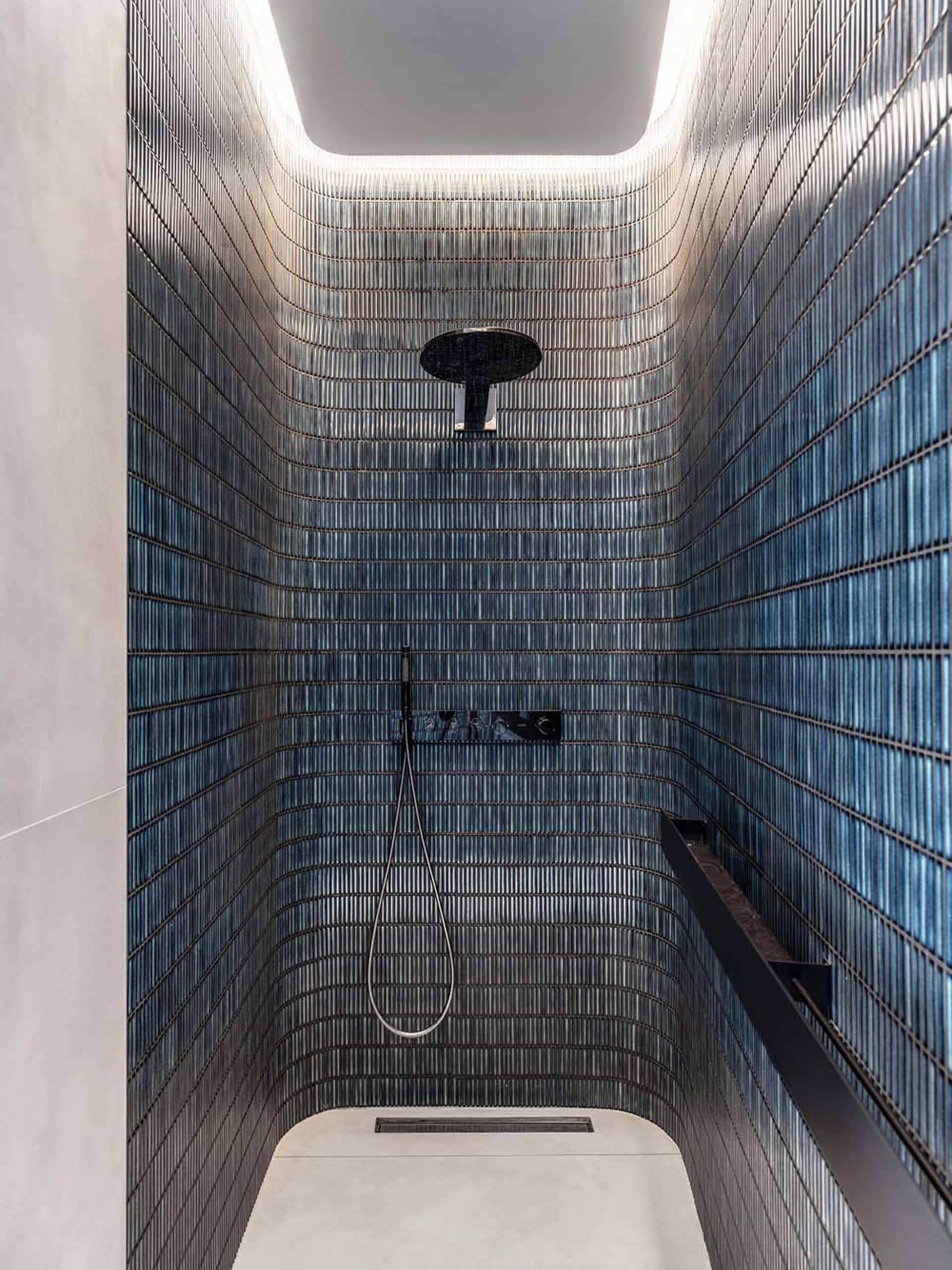 A minimalist bathroom with glass tiles, featuring a shower area with a ceiling light and a hand-held showerhead.