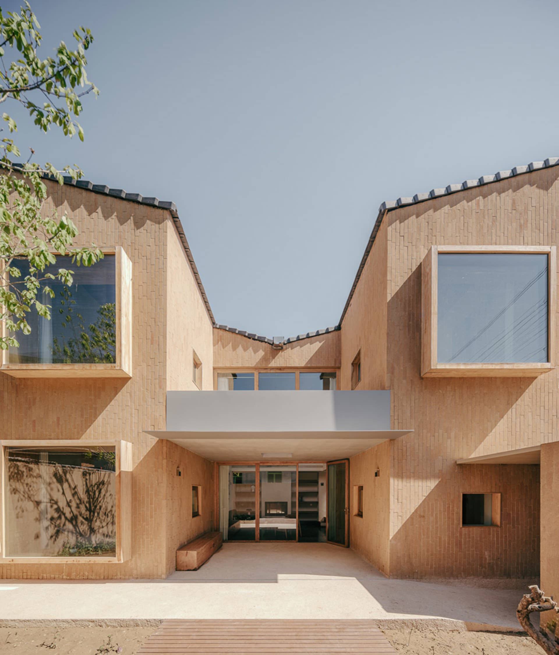 A modern building facade made of clay with large windows and a concrete awning.