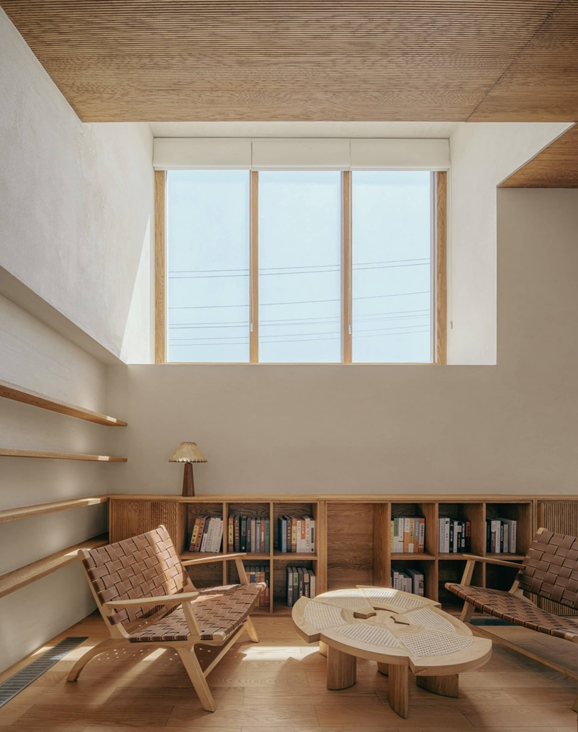 A minimalist living room with wooden furniture and shelves, featuring a window and a table.