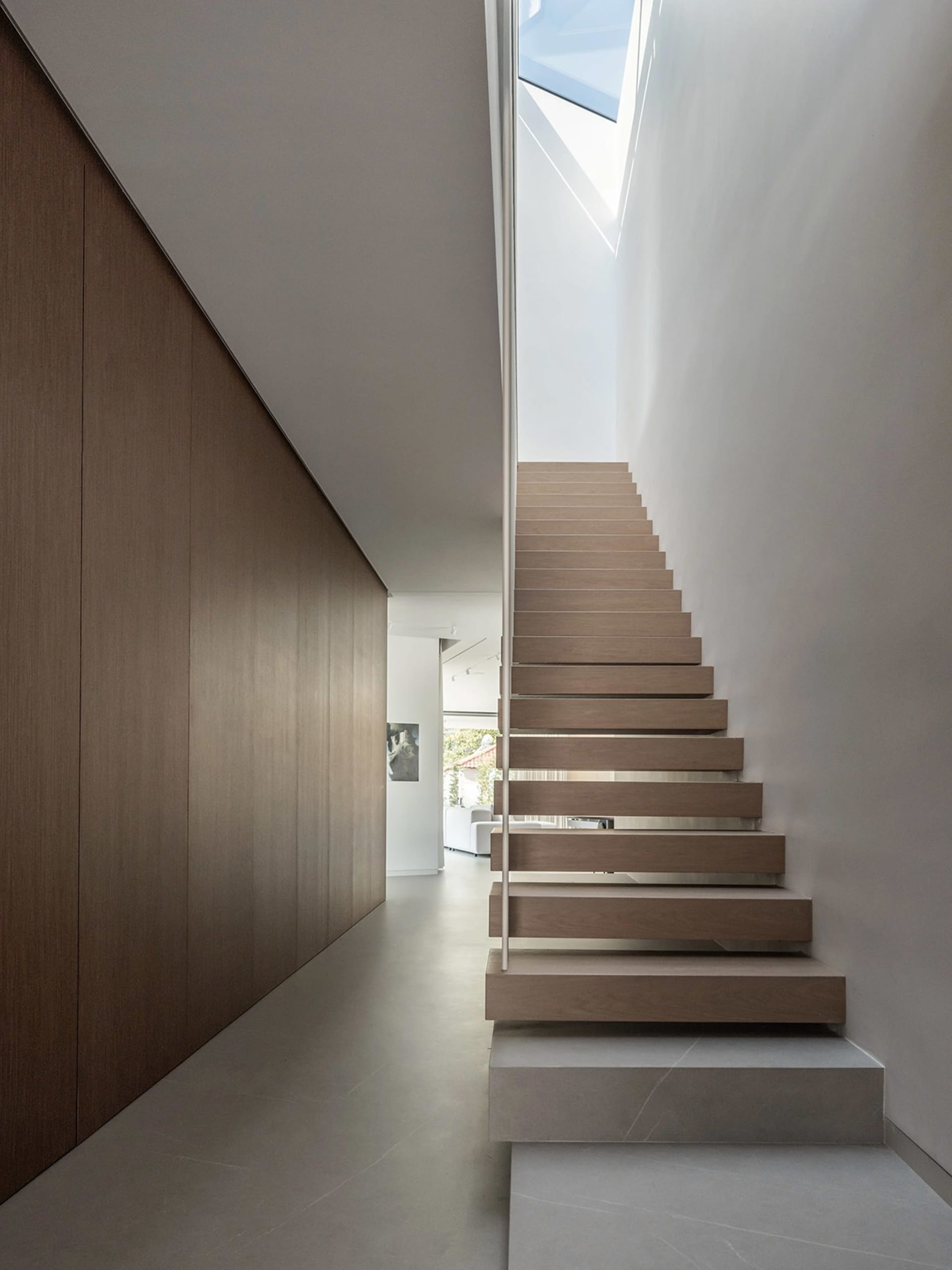 Modern minimalist wooden staircase with a sleek railing and natural light coming through a skylight.