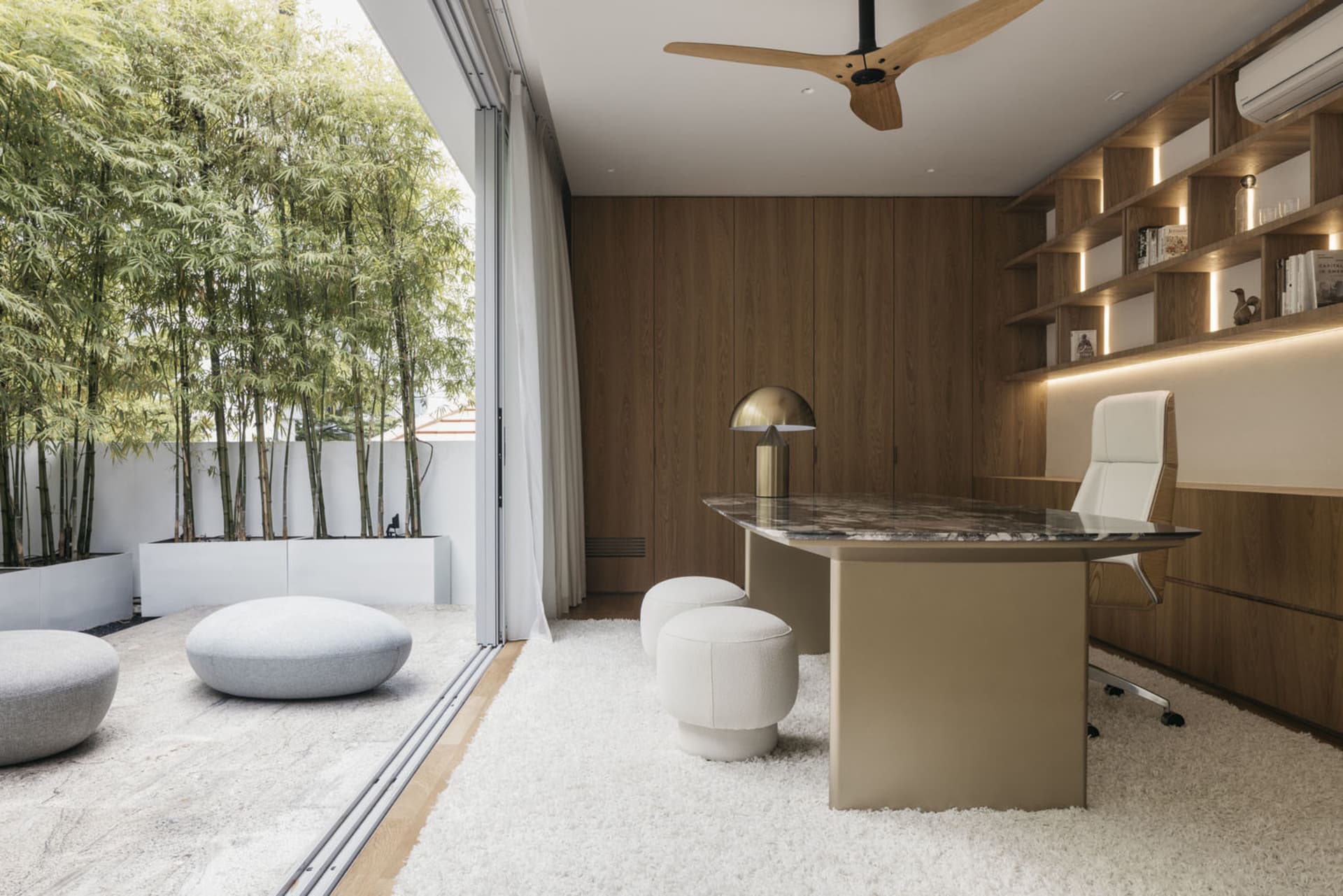 Modern office space featuring a marble desk, wooden cabinets, and white upholstered seating.