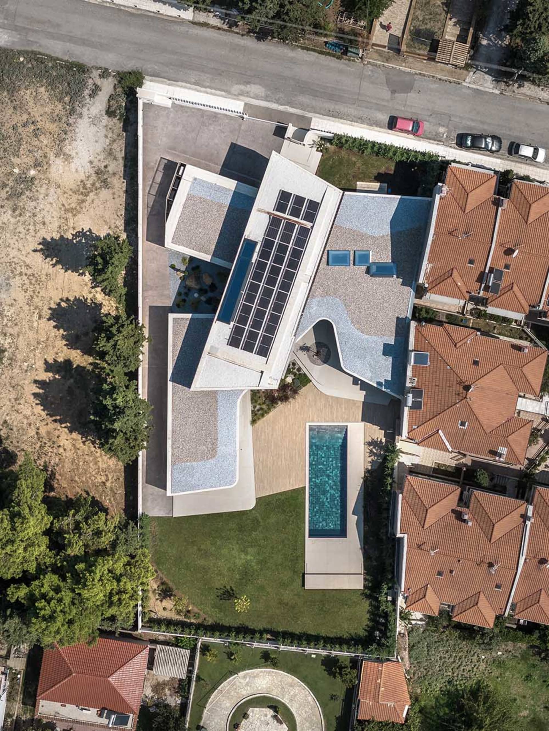 Aerial view of a modern residential house with a concrete roof and solar panels.