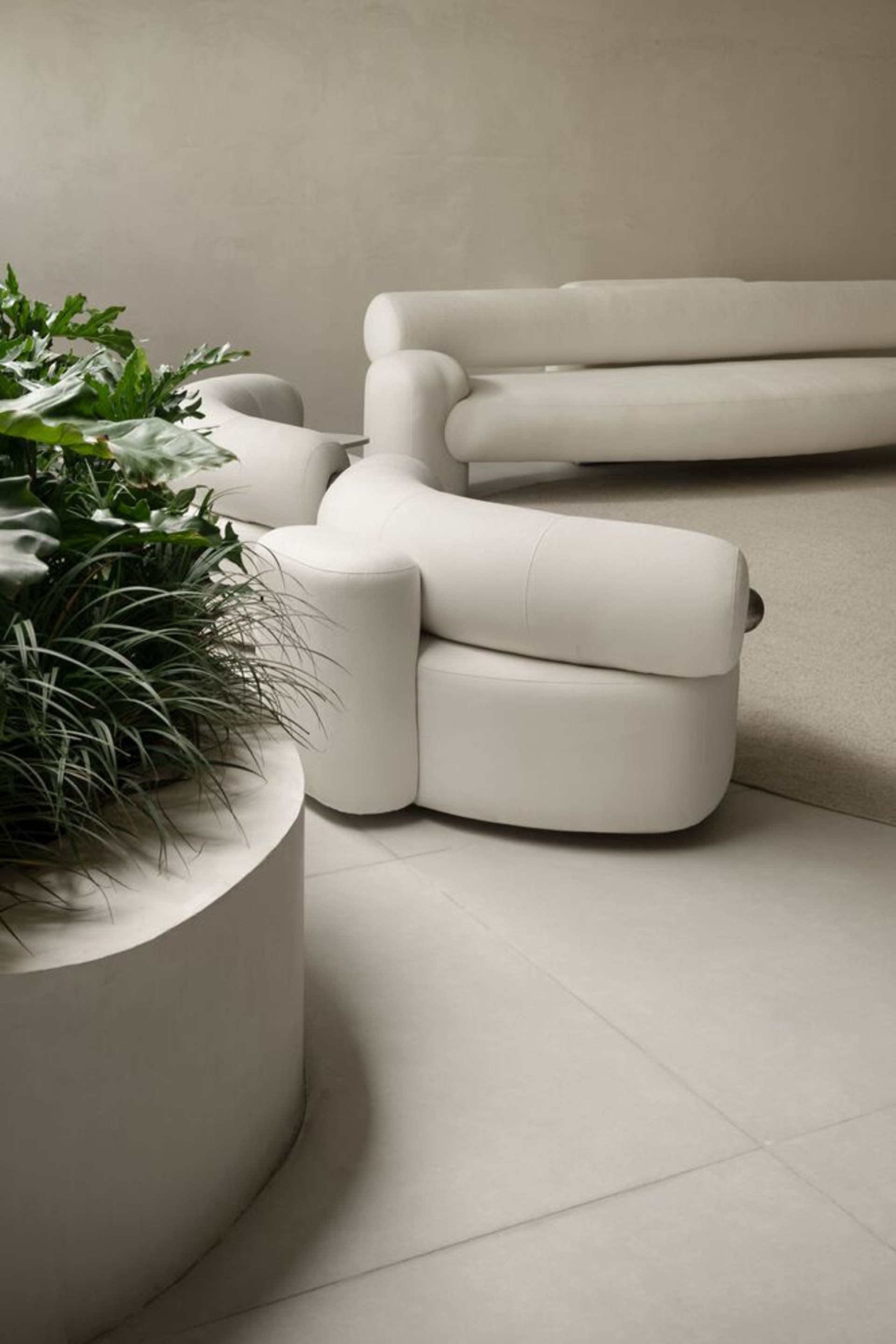 A modern white sofa with circular base and a matching white circular planter with green plants next to it.