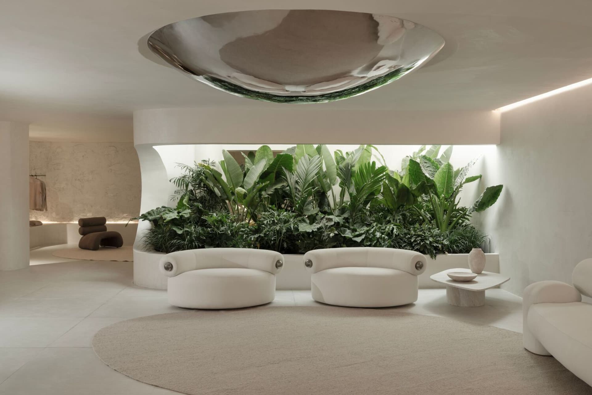 Modern interior design featuring white leather sofas and a circular coffee table with green plants in the background.