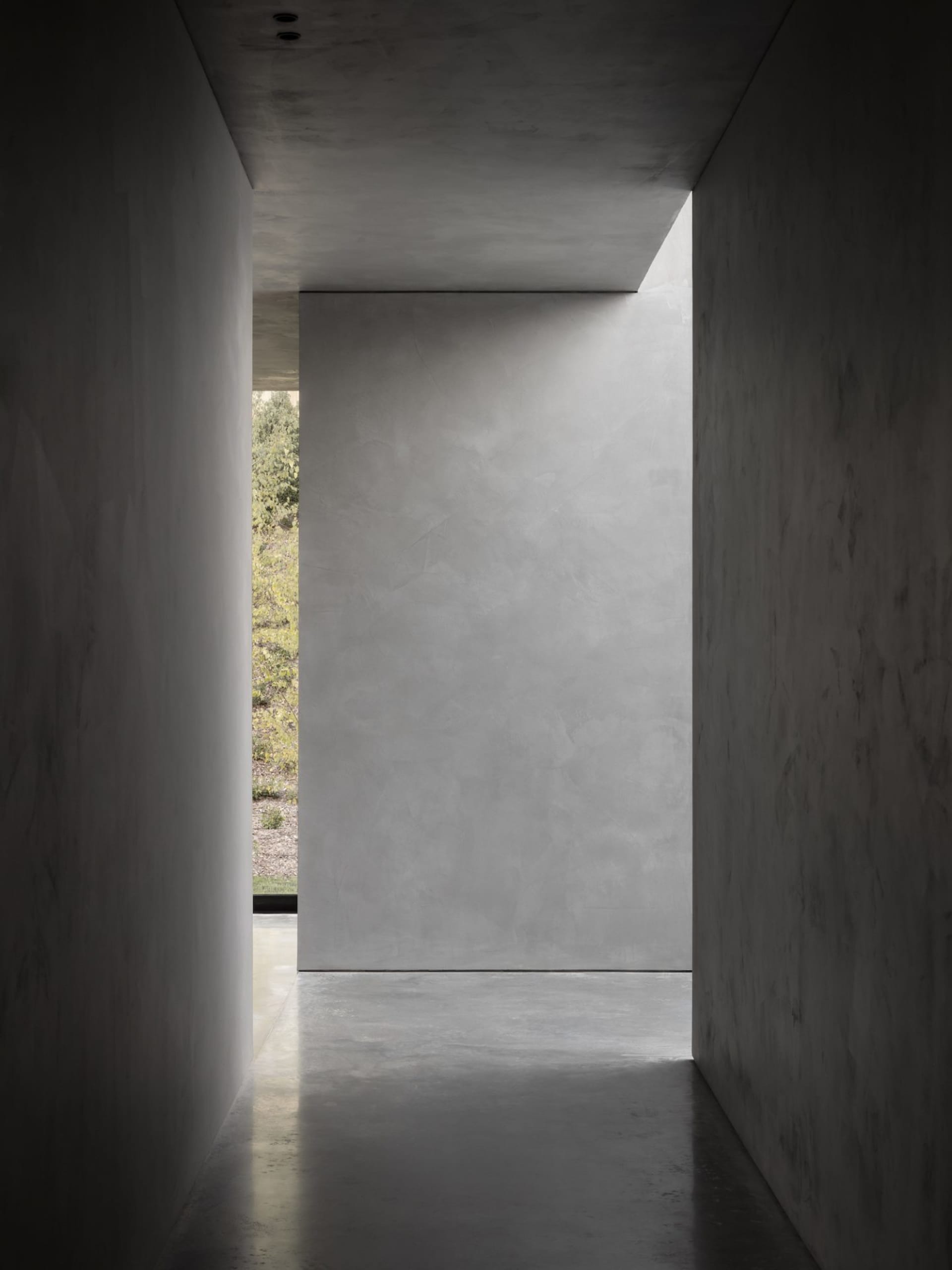 Minimalist interior with concrete walls, floors, and ceilings, leading to a natural light-filled space.