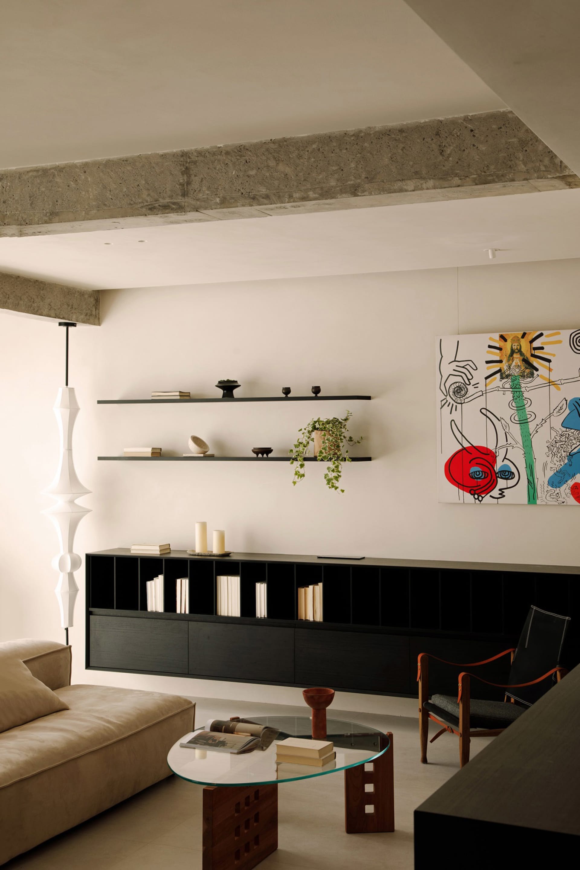 A modern living room with floating concrete shelves containing various decorative items and books, a beige sofa, a glass coff