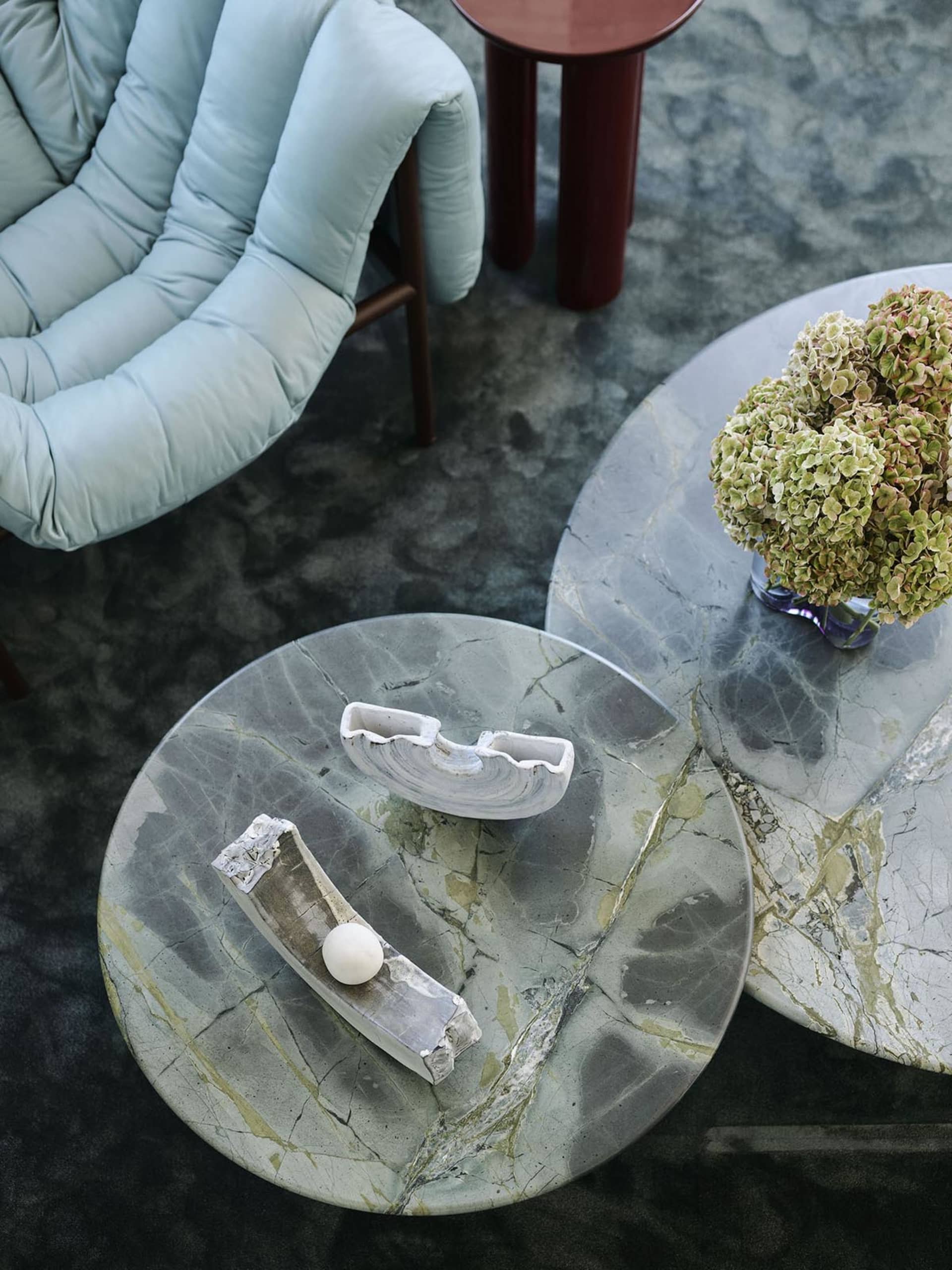 一間現代客廳,擺放大理石茶几,搭配裝飾性混凝土雕塑與一瓶繡球花。