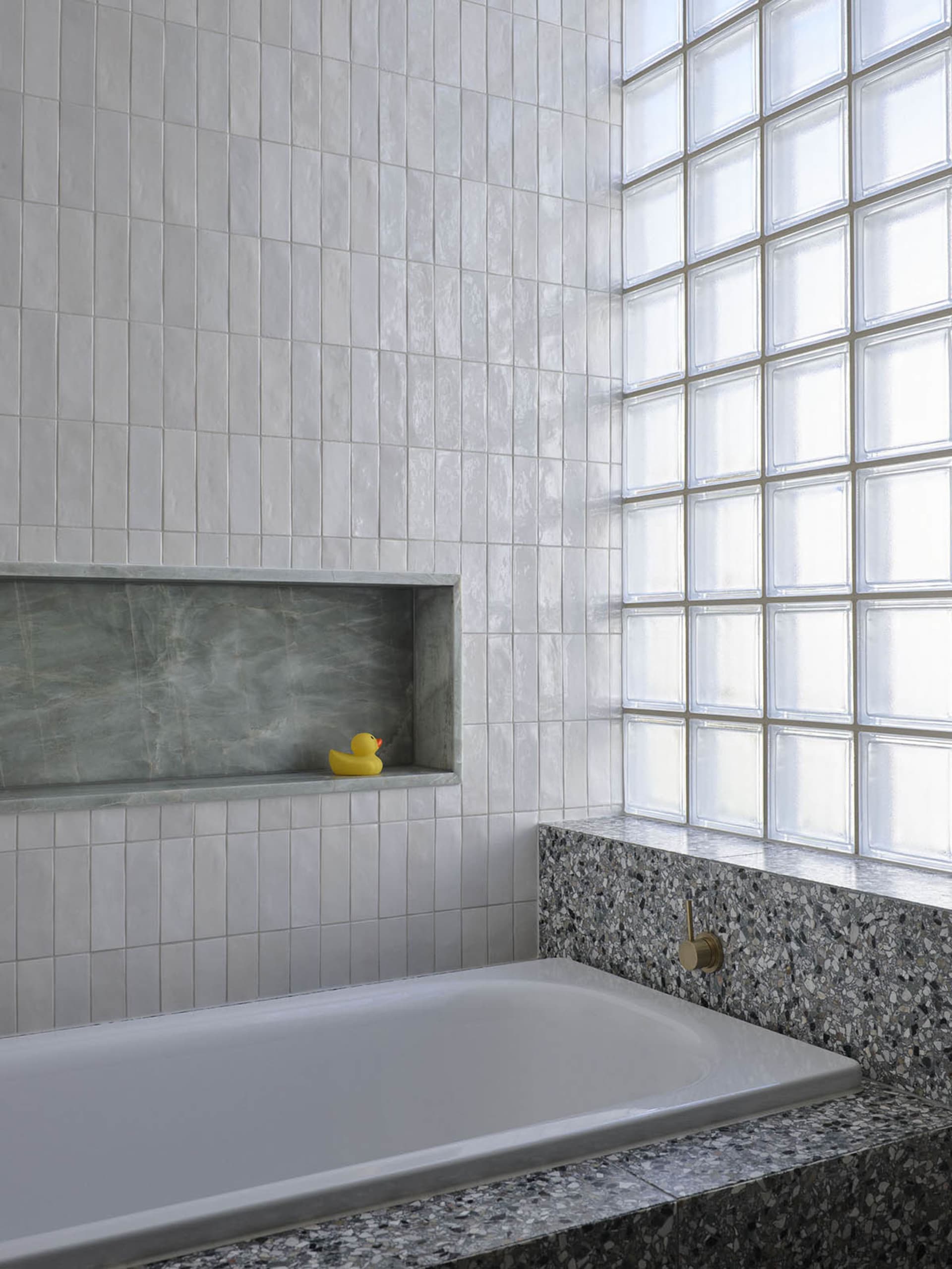 Modern bathroom interior featuring white terrazzo tiles, white bathtub, and a window with clear glass.