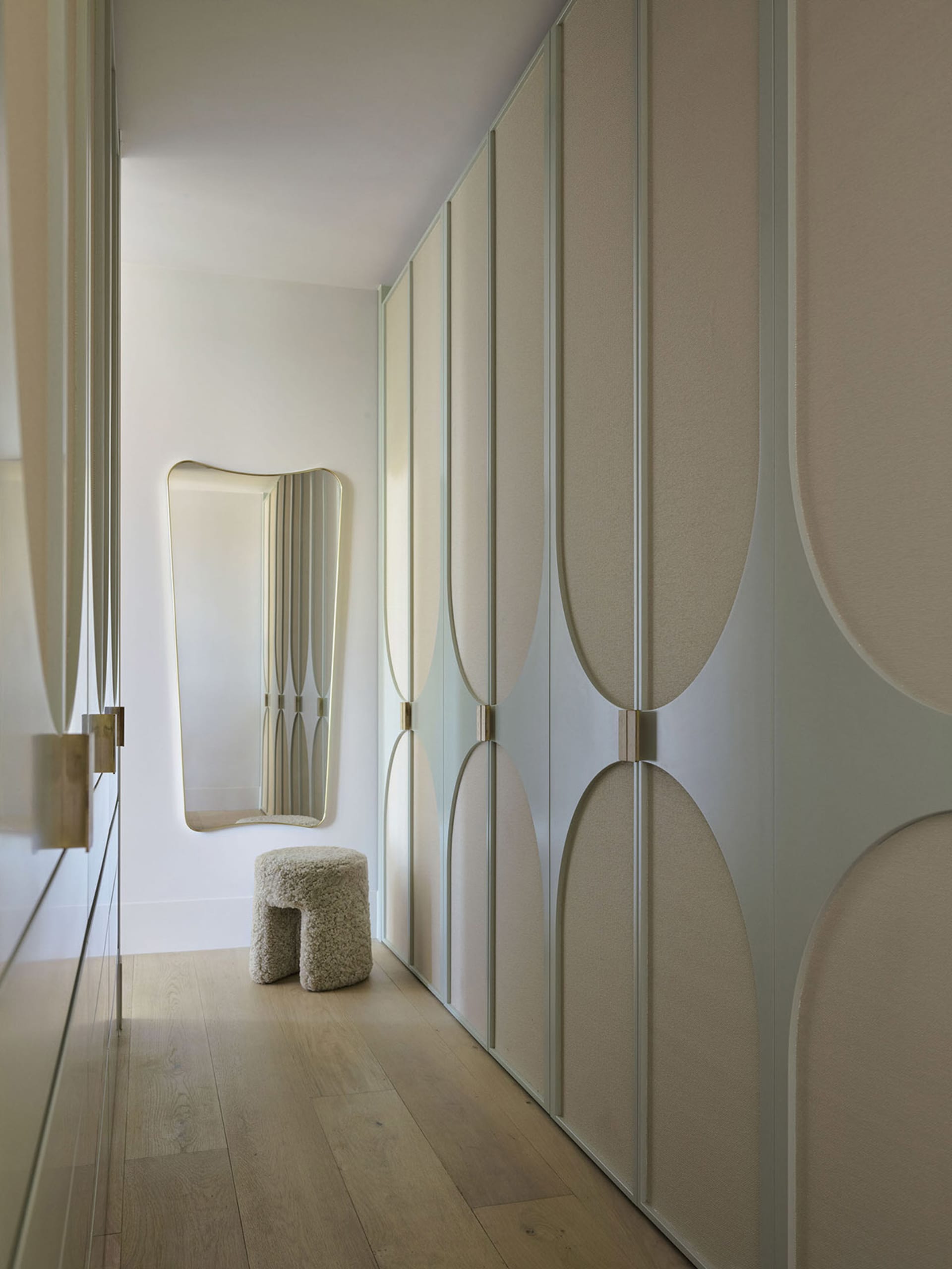Modern closet with linen fabric wall covering, circular door designs, and a stool with a textured surface.