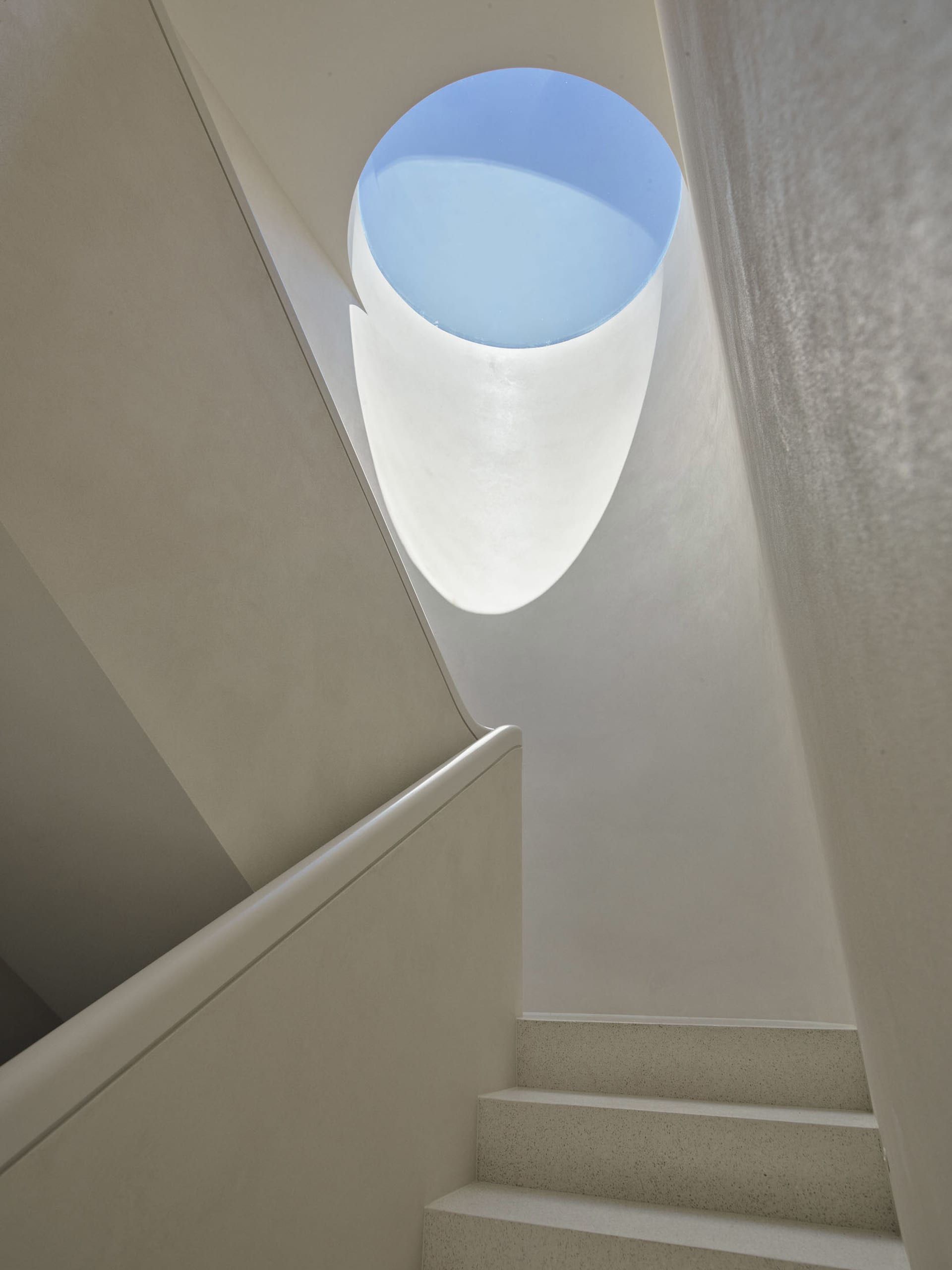 A minimalist staircase made of concrete, featuring a circular window at the top.