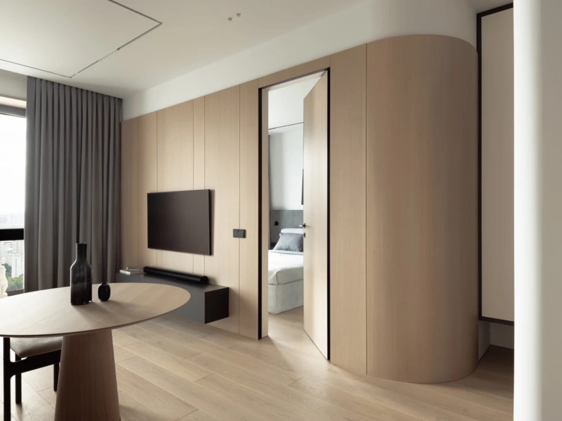 A modern minimalist living room with a round wooden table and curved wooden cabinet.