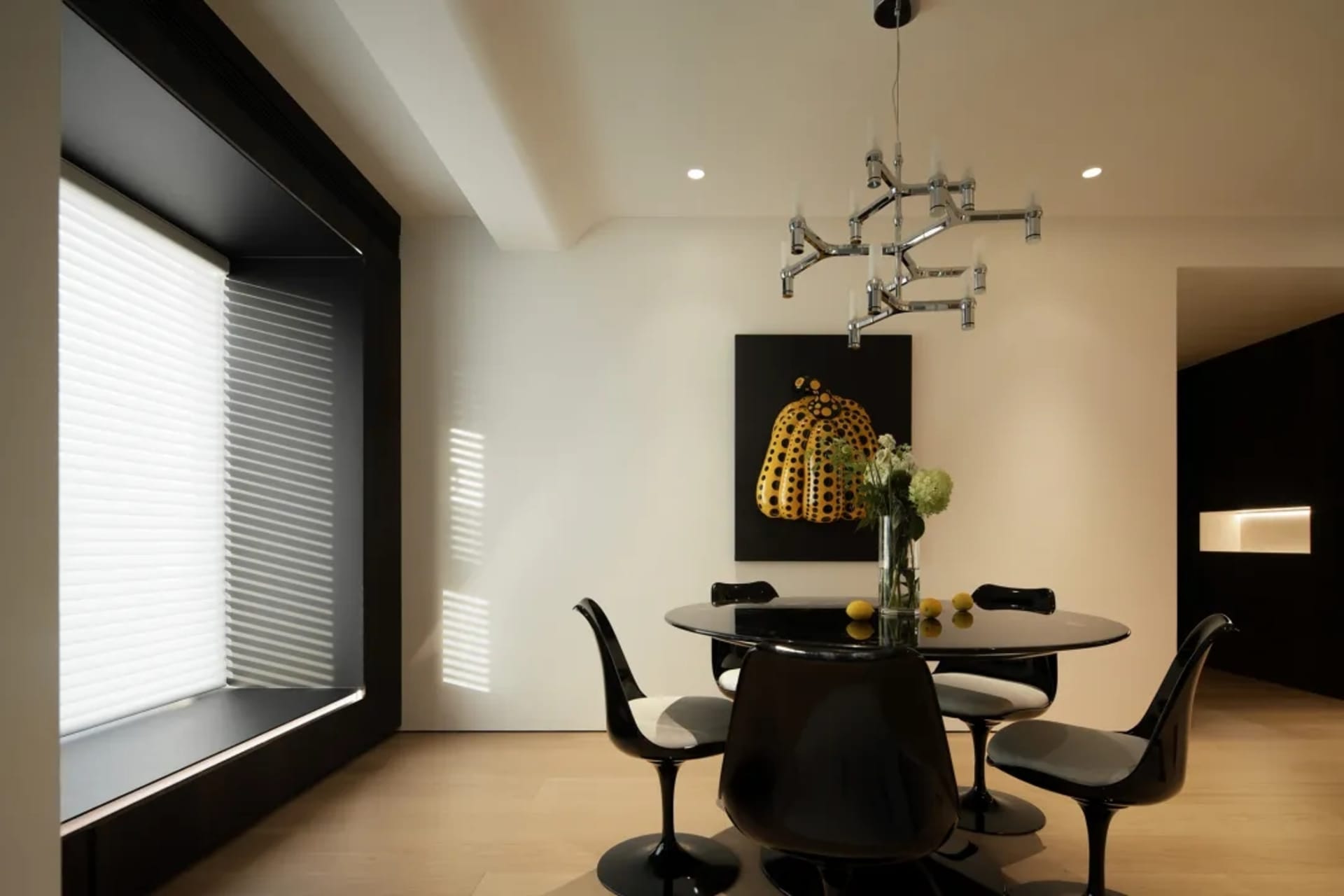 Modern minimalist dining room featuring a glass table with black and white chairs, a chandelier, and a black and yellow abstr