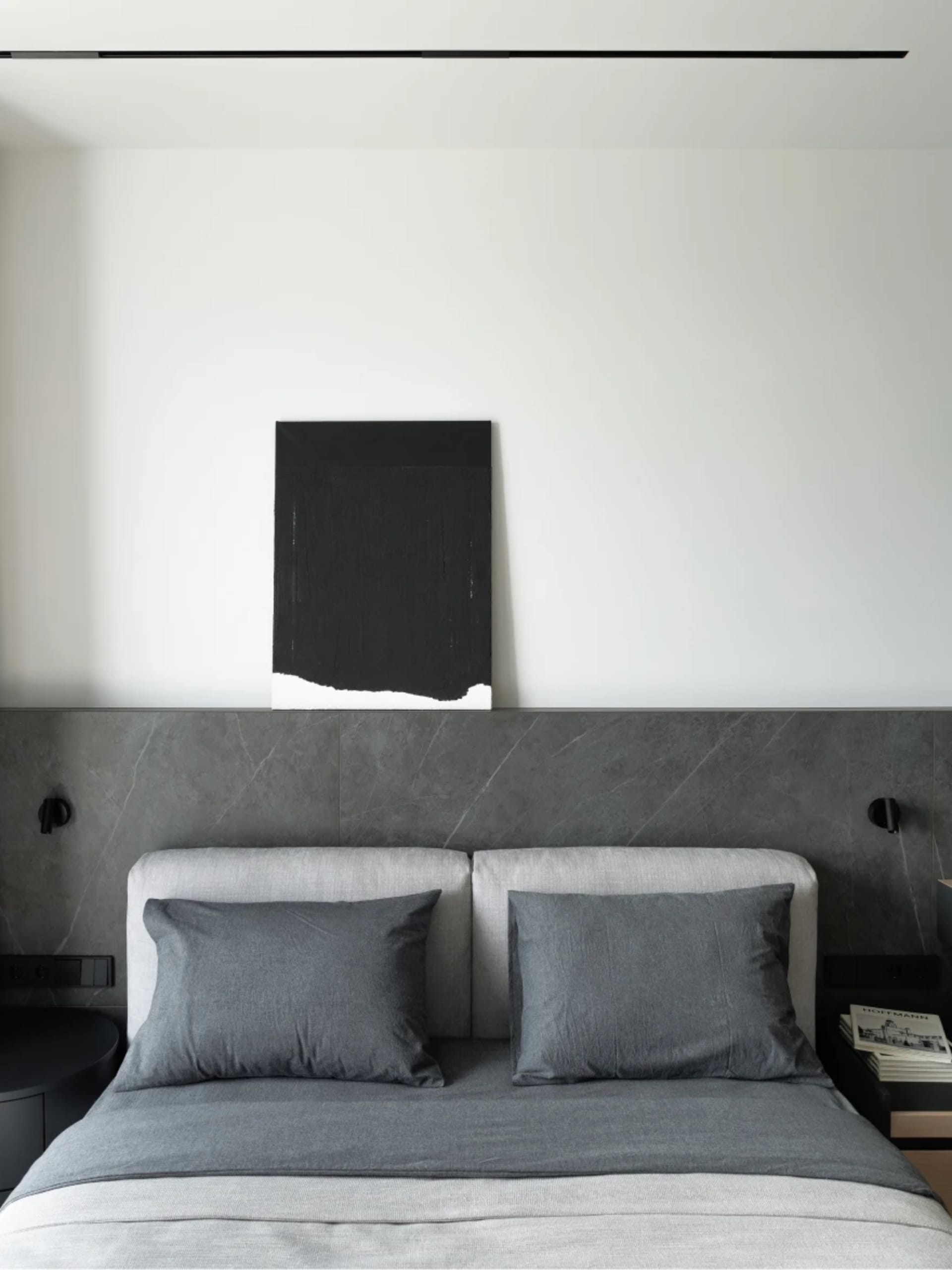 Minimalist bedroom with concrete headboard, metal accents, and gray fabric bedding.