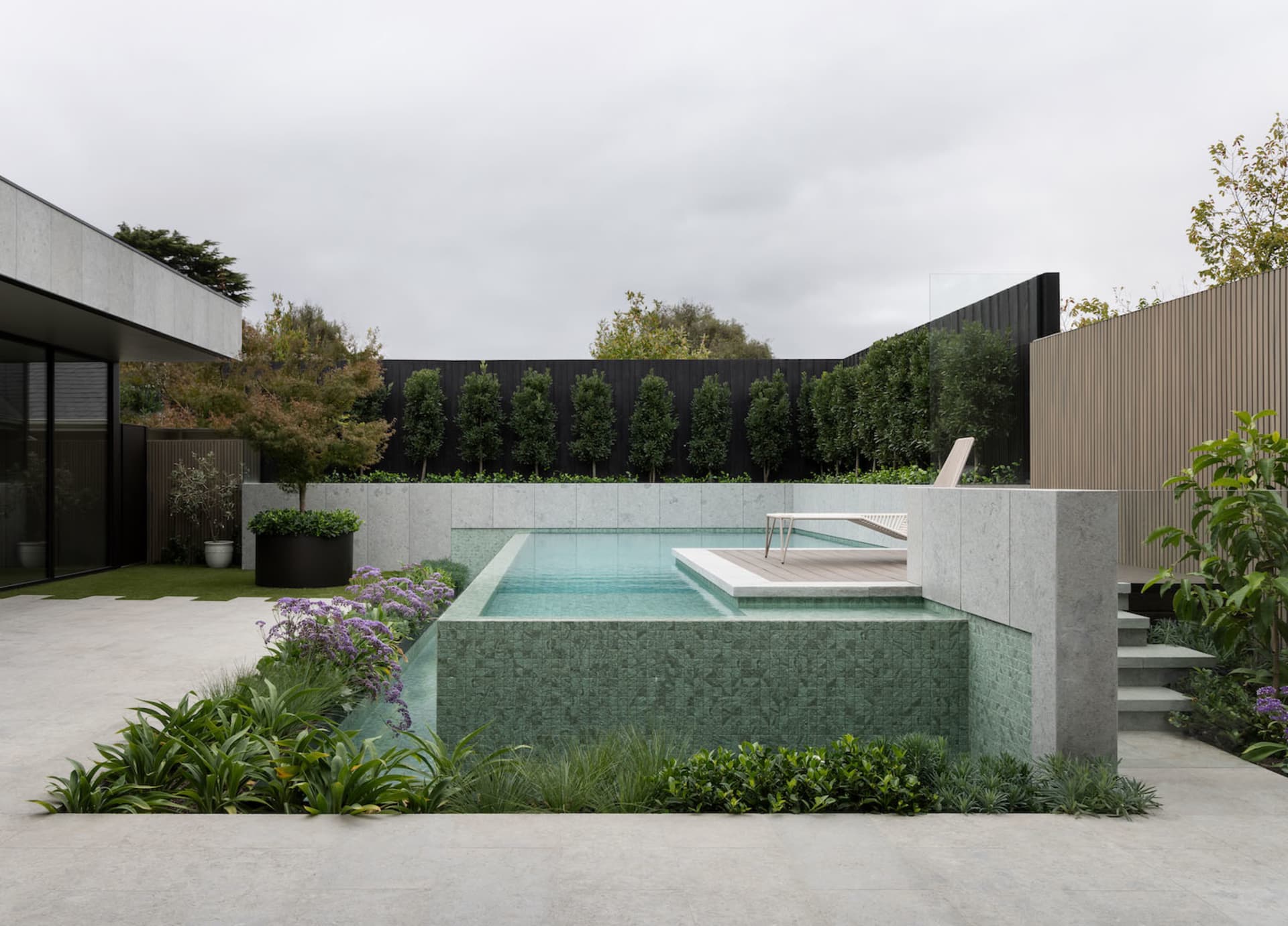 Modern minimalist residential outdoor space featuring a sleek concrete pool and well-manicured garden.
