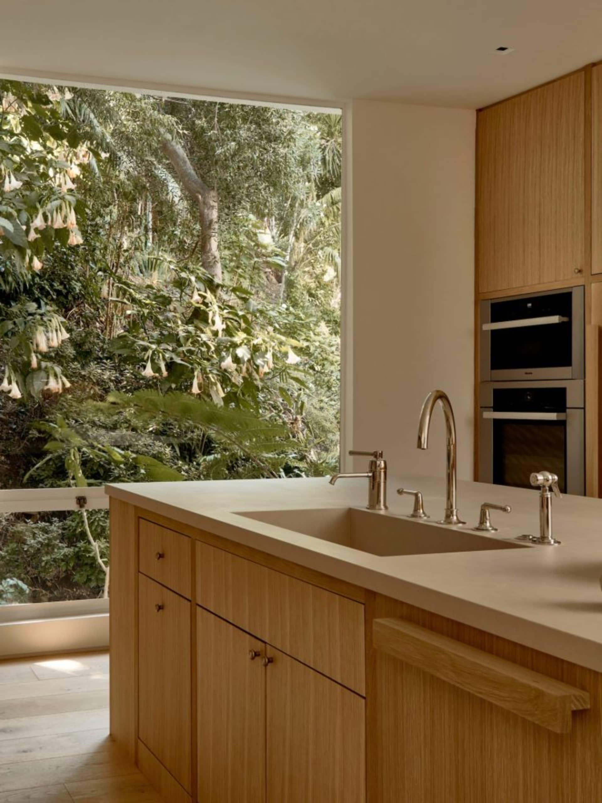 A modern kitchen with wooden cabinets and a large window overlooking a lush green garden.