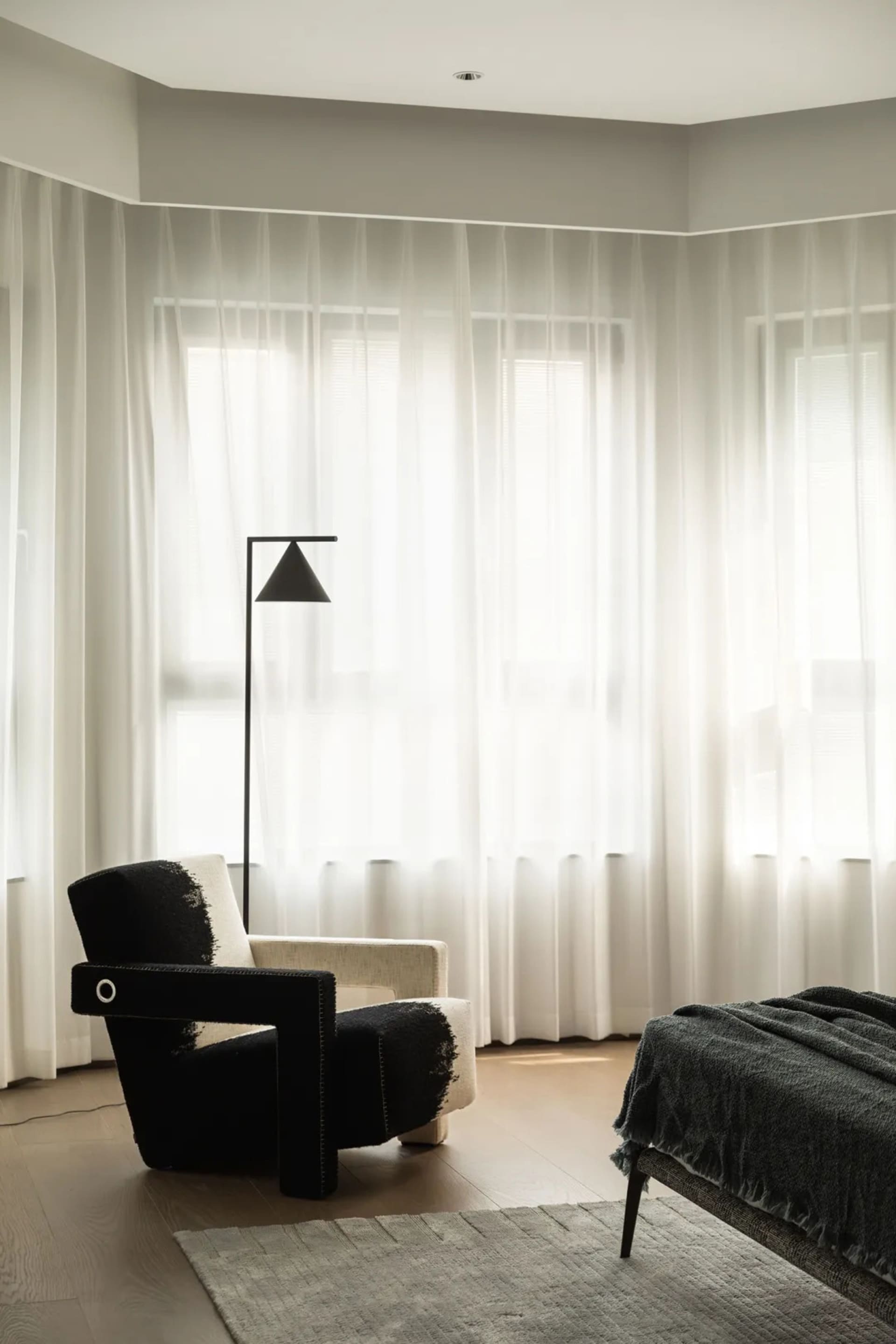 A modern bedroom featuring sheer white curtains allowing natural light to filter through.