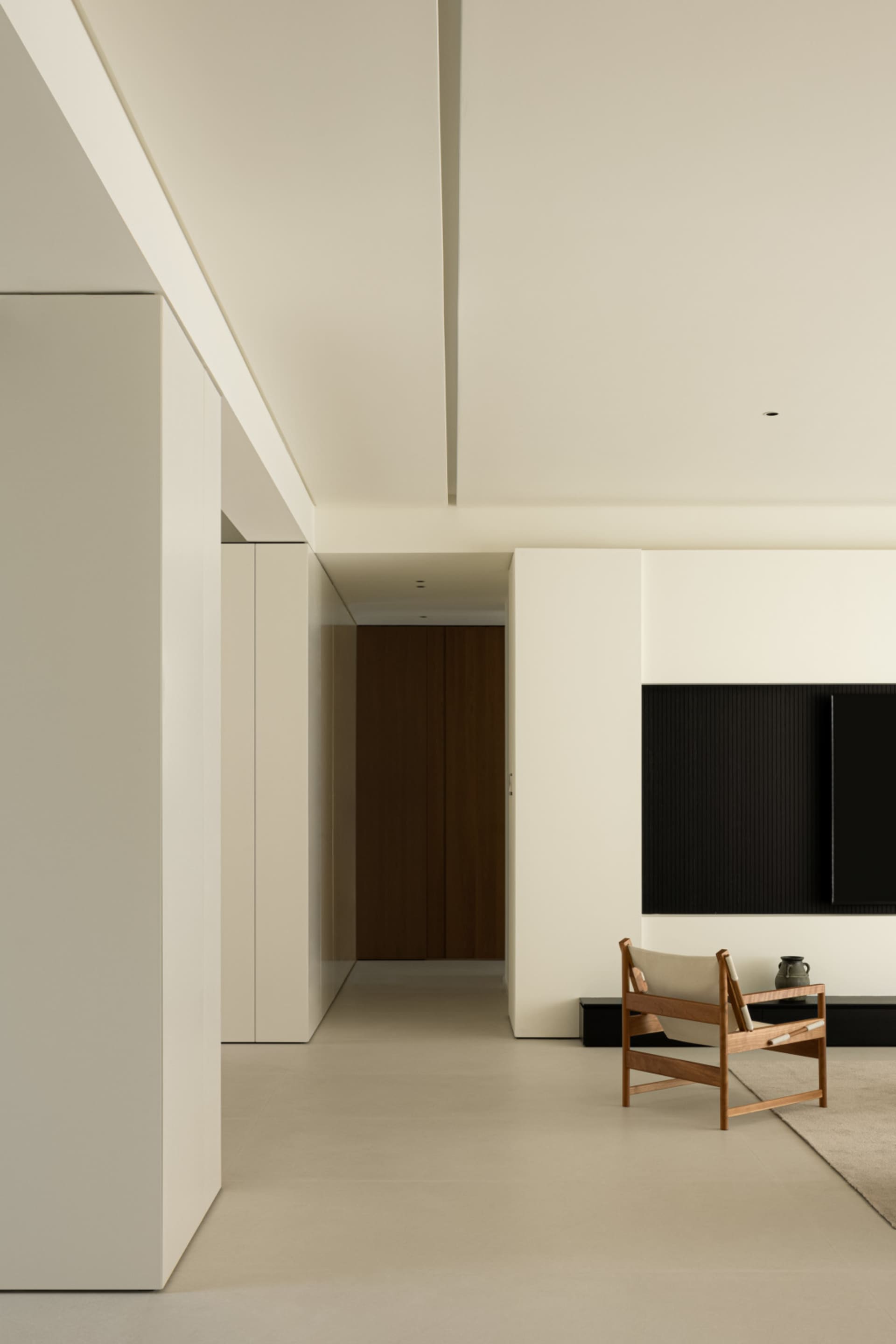 A minimalist living room featuring concrete walls and flooring, with a wooden chair and black television setup.